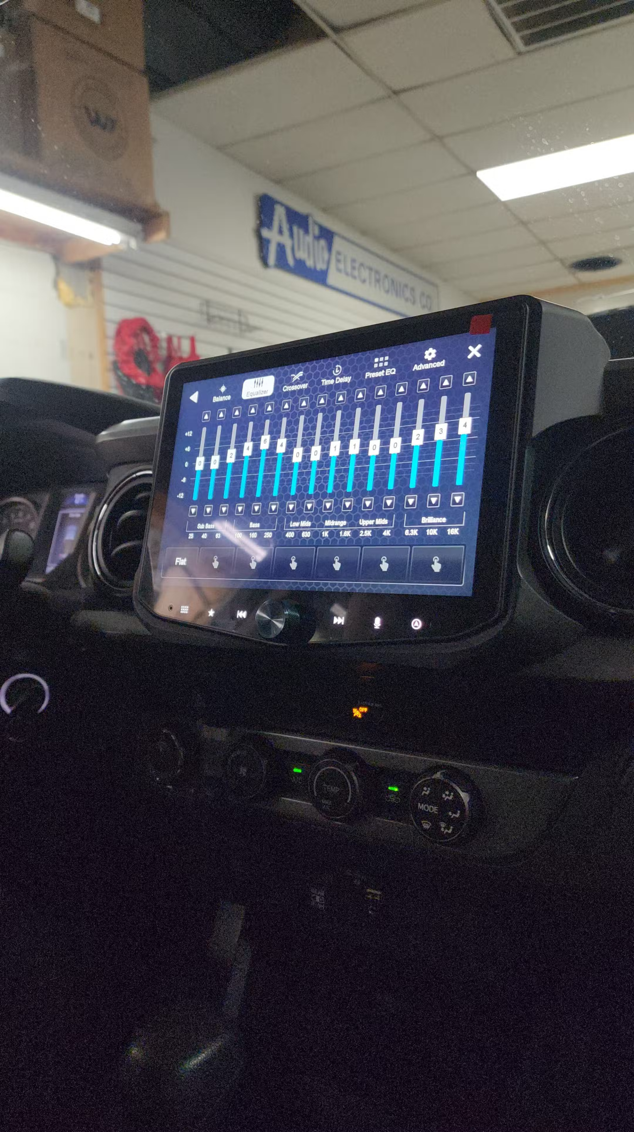 Aftermarket touchscreen stereo mounted in a truck dash displaying a graphic equalizer screen inside a shop bay