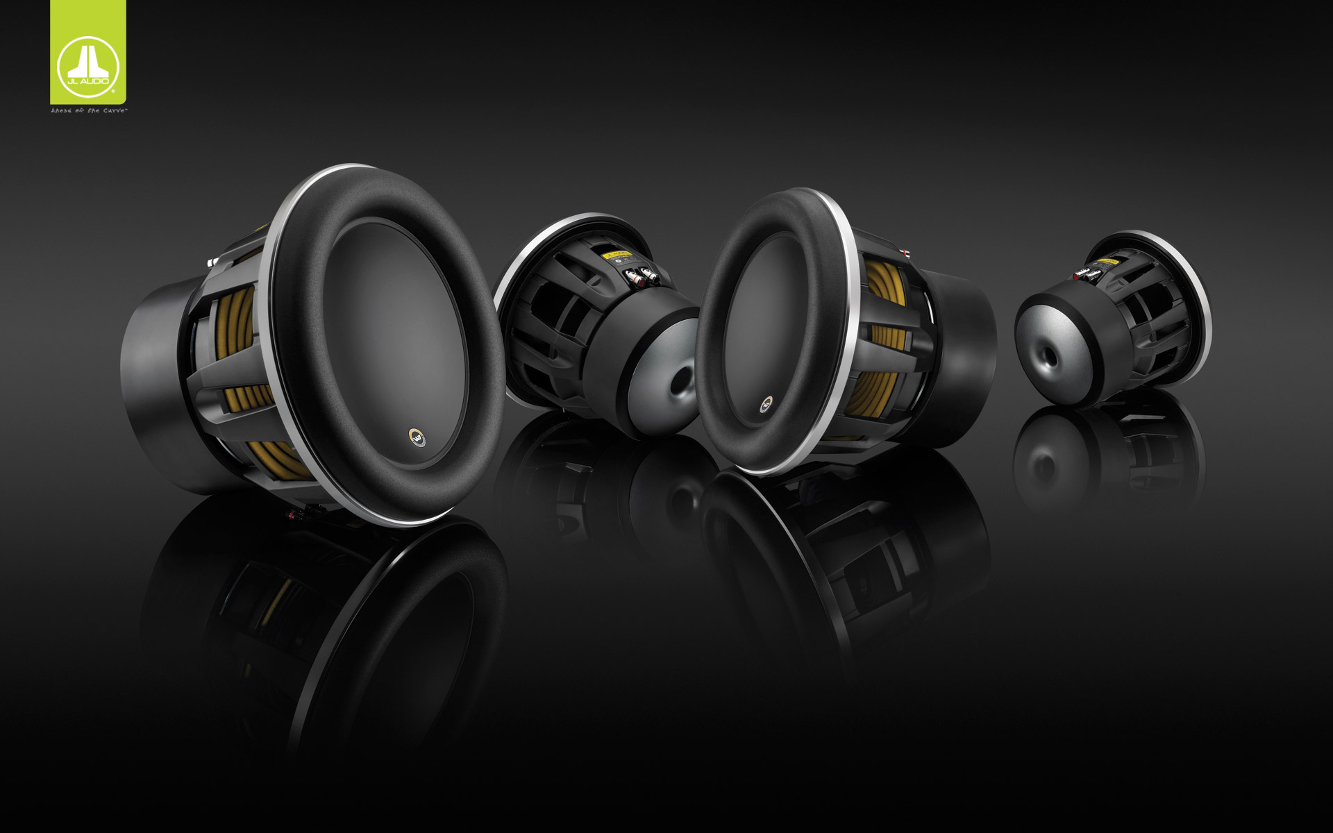 Four car subwoofer drivers in different sizes arranged on a glossy black surface in a studio product shot.