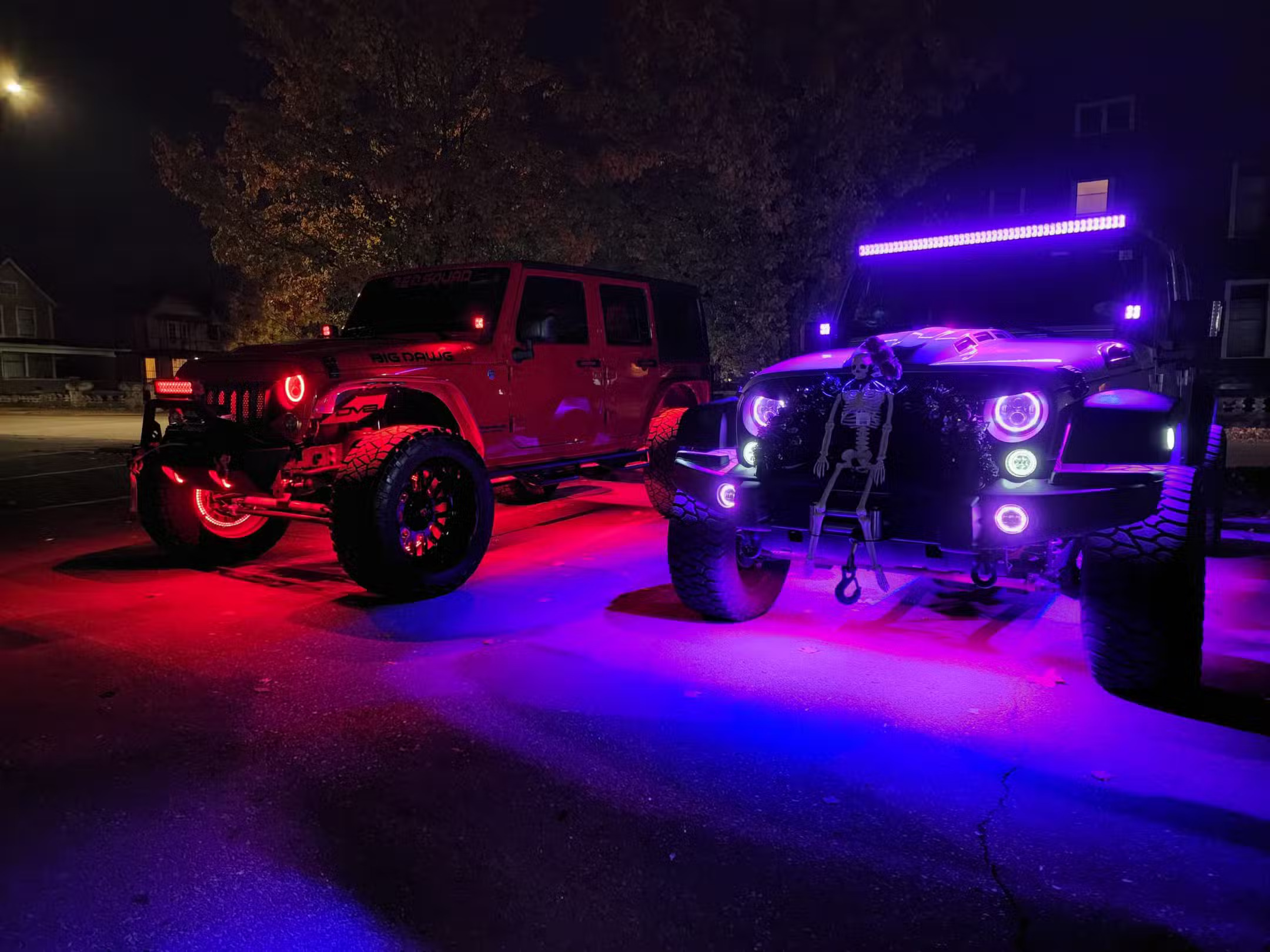 Two lifted Jeeps parked at night with red and purple underglow and glowing halo headlights.