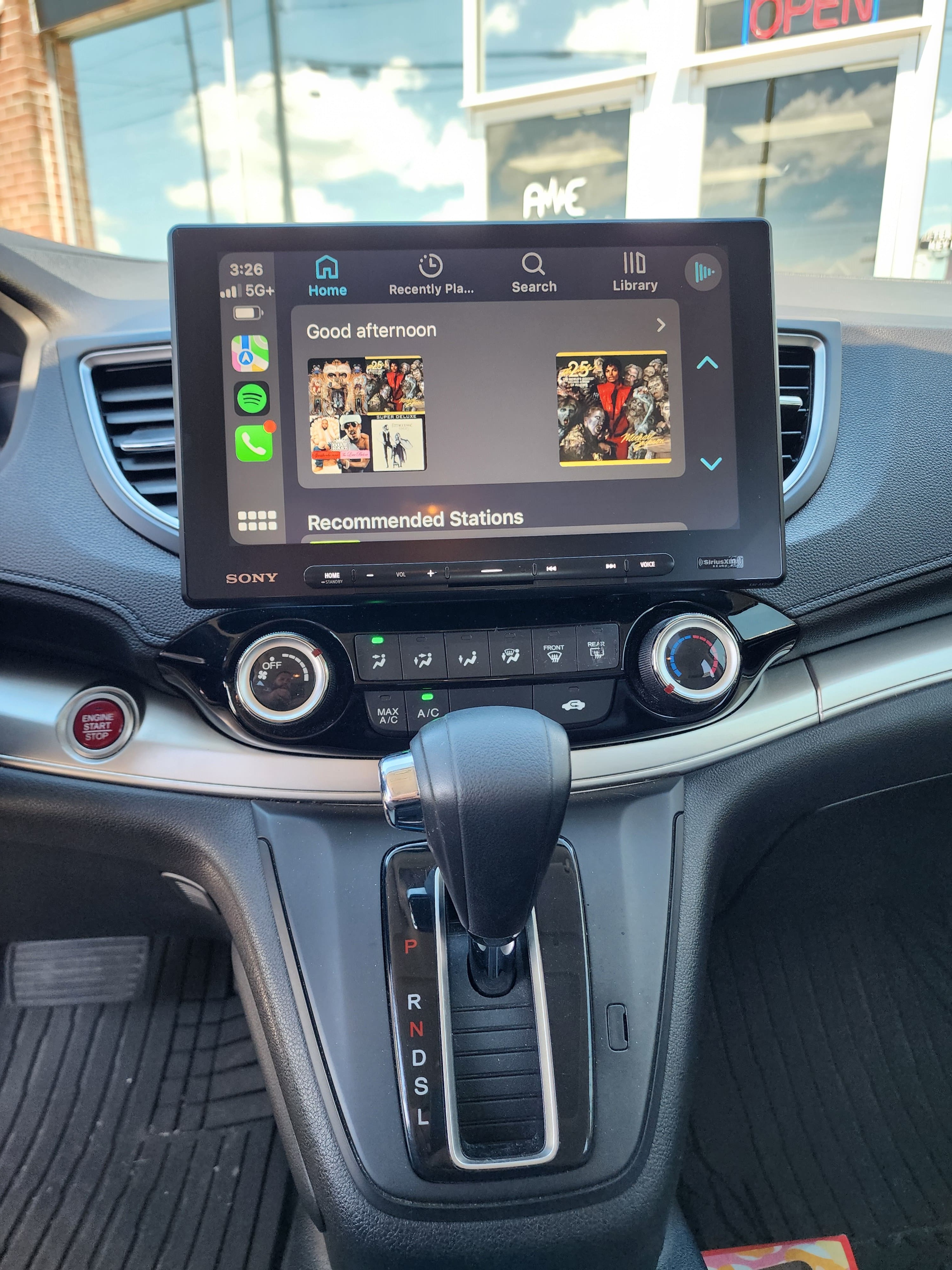 Large floating touchscreen receiver installed in a Honda dash showing a music app menu above the shifter