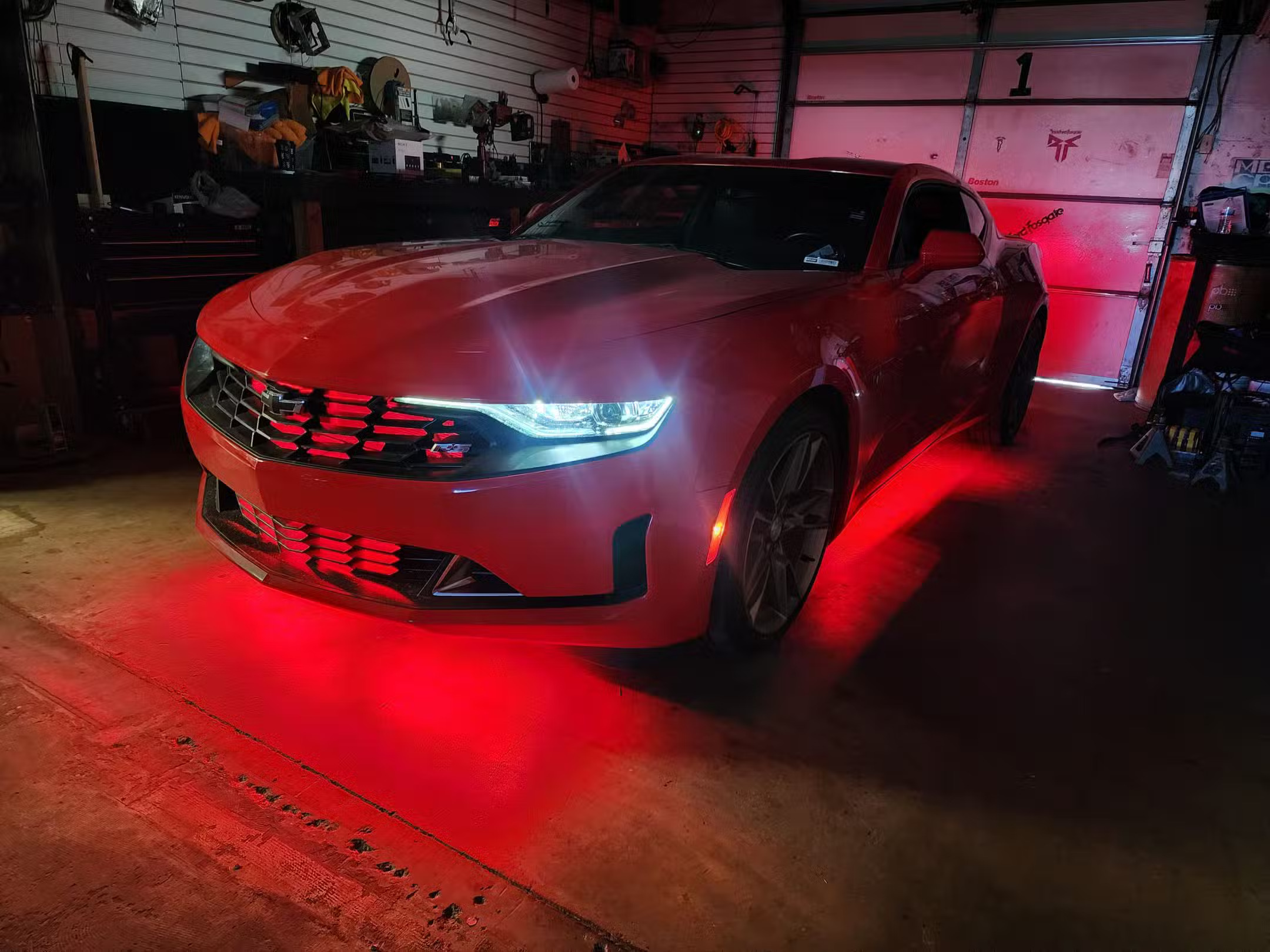 Red Chevrolet Camaro in a garage bay with red underglow and illuminated grille accent lighting.