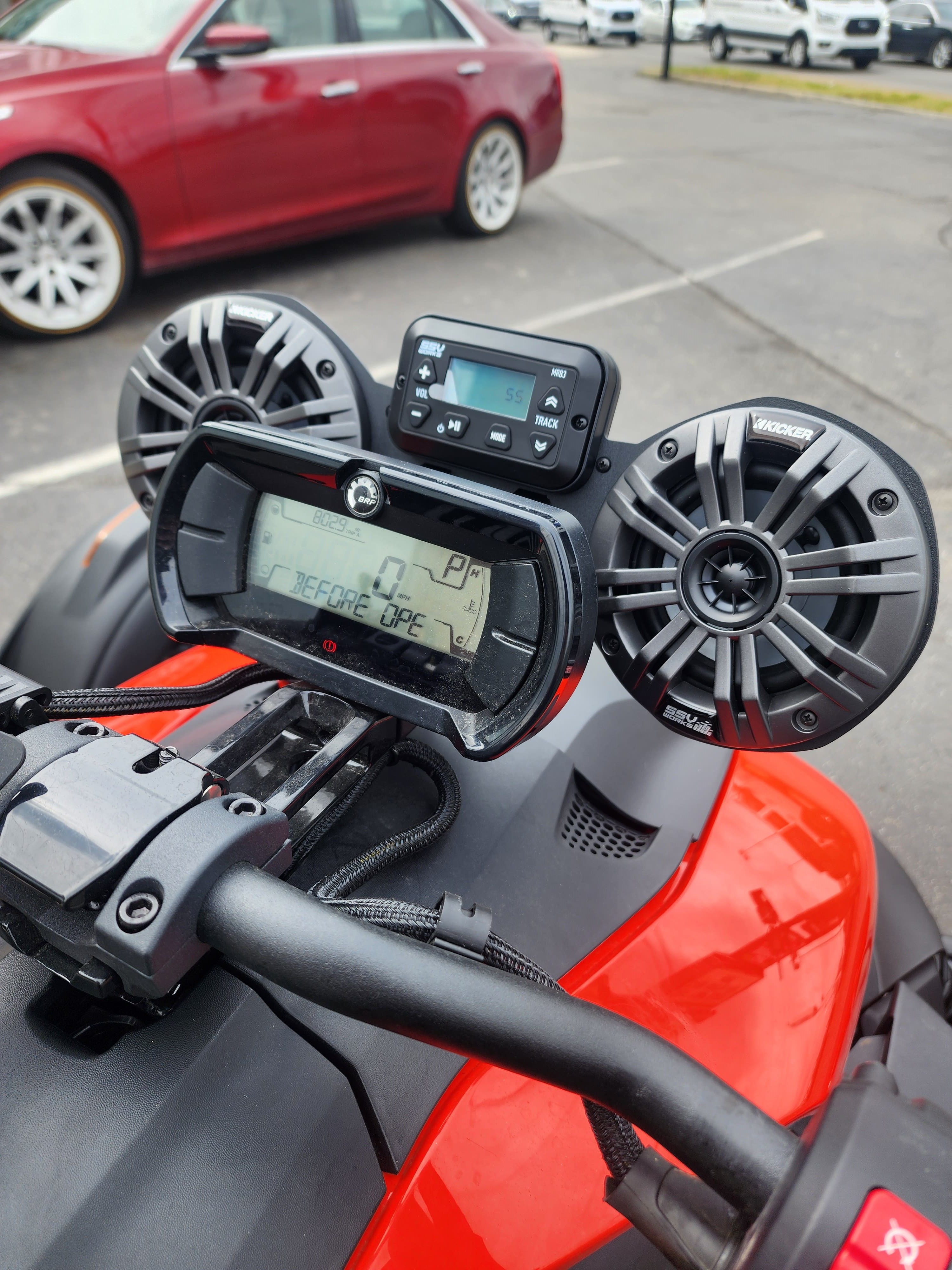 Pair of handlebar pod speakers and a weather resistant stereo receiver mounted above the gauges on a red ATV.