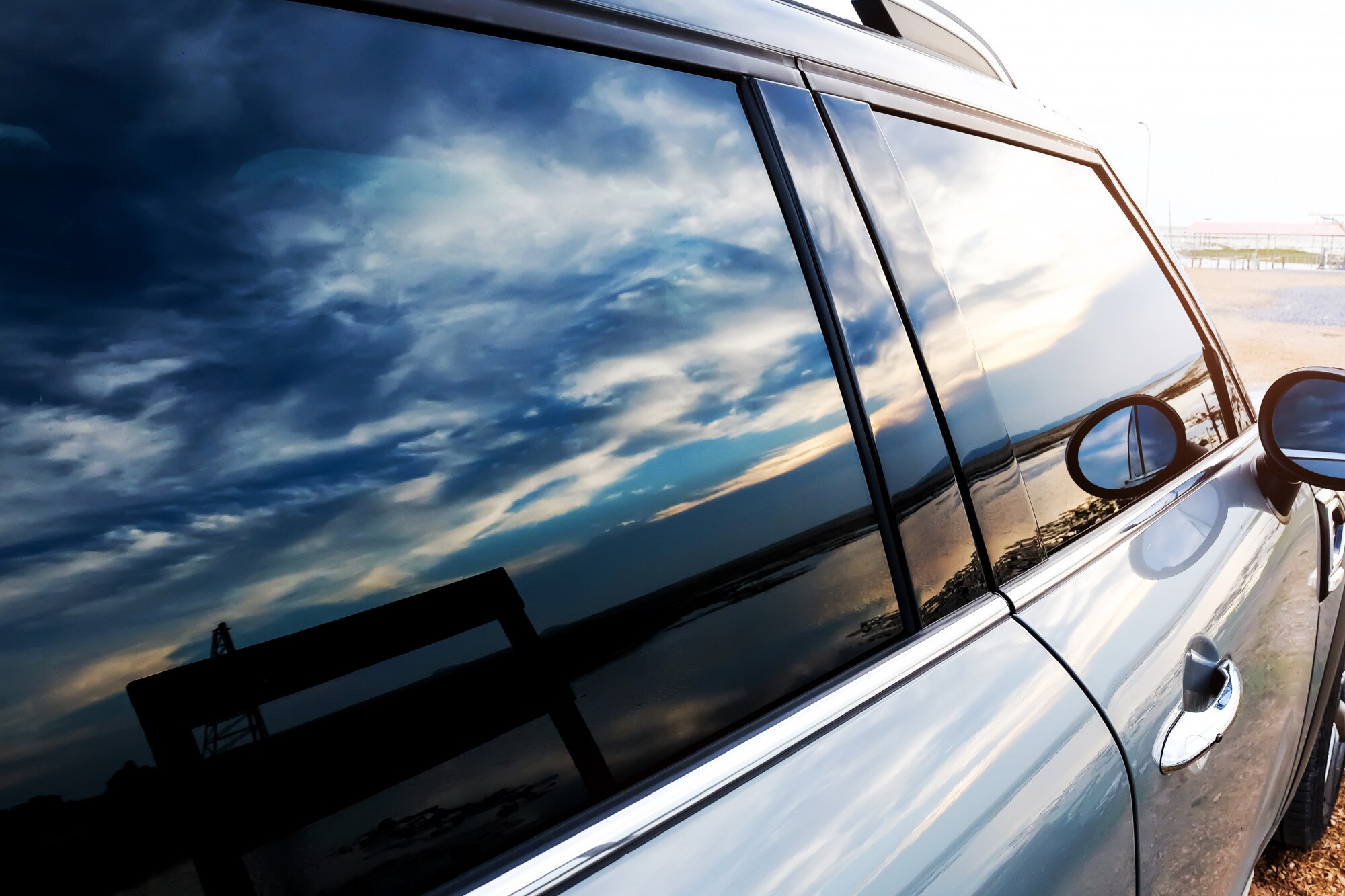 Dark tinted side windows on a silver SUV reflecting a dramatic cloudy sky at dusk.