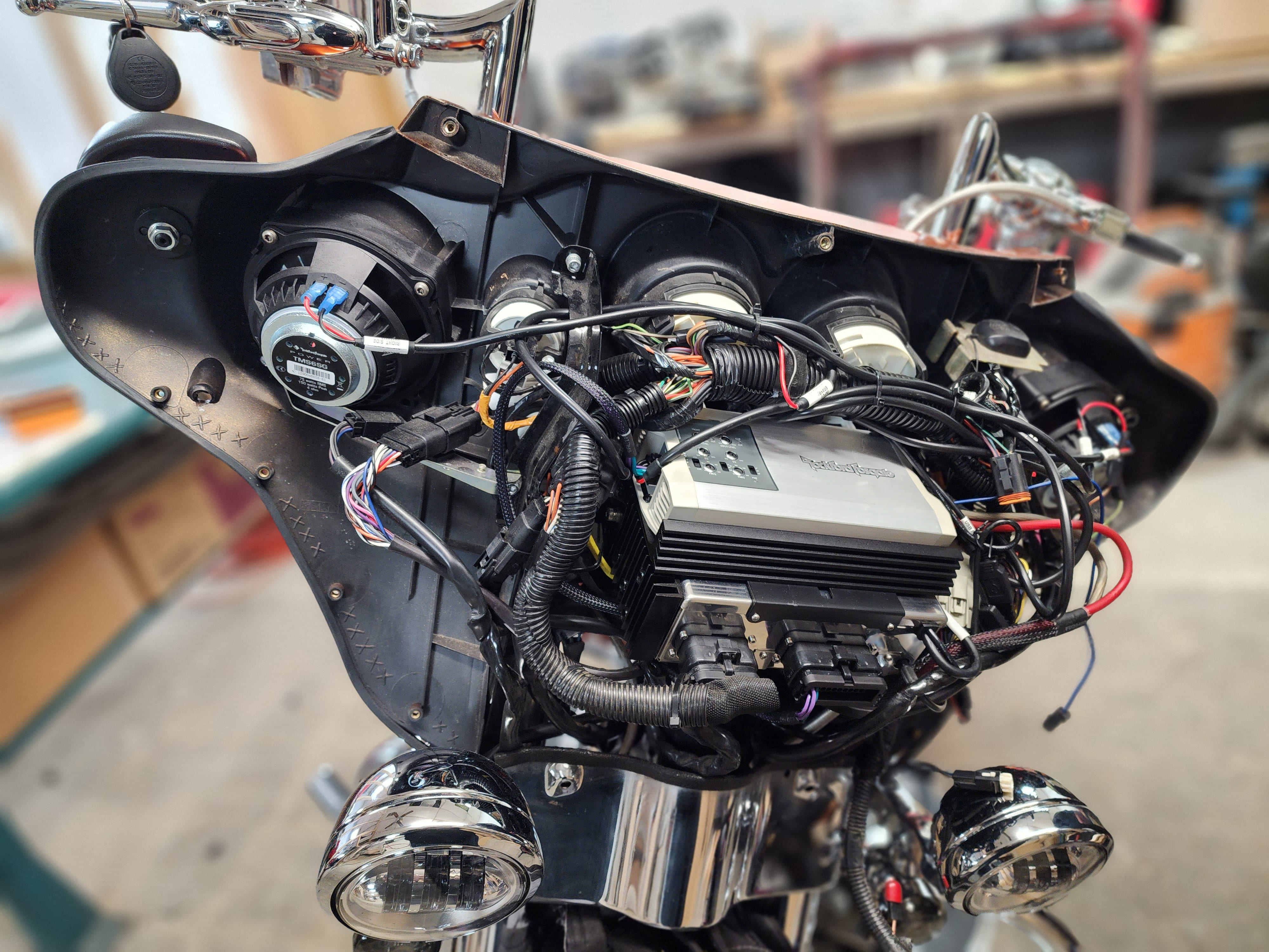 Motorcycle batwing fairing opened up on a bench, showing a mounted amplifier, speakers and bundled wiring harnesses.