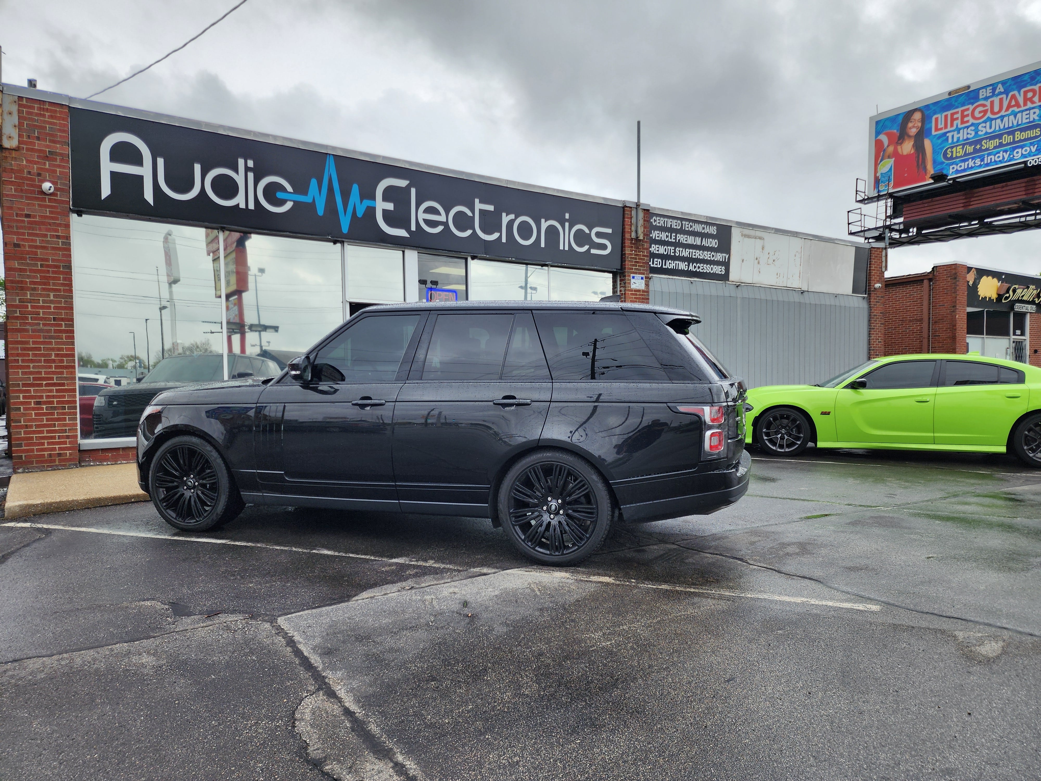 Black SUV parked outside the Audio Electronics shop, with the lit storefront sign above the windows.
