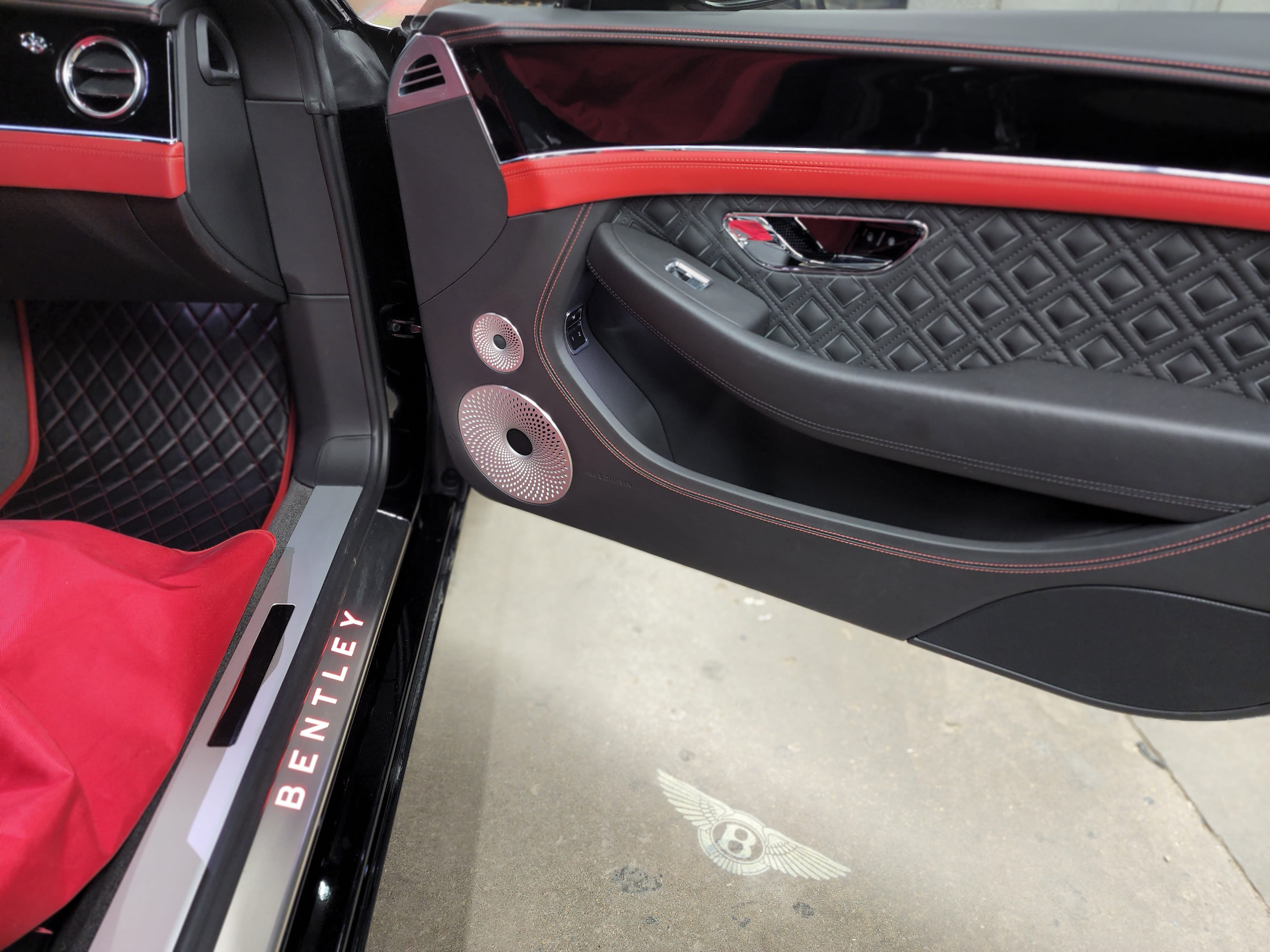 Open door of a black and red Bentley showing a quilted leather panel with a polished speaker grille.