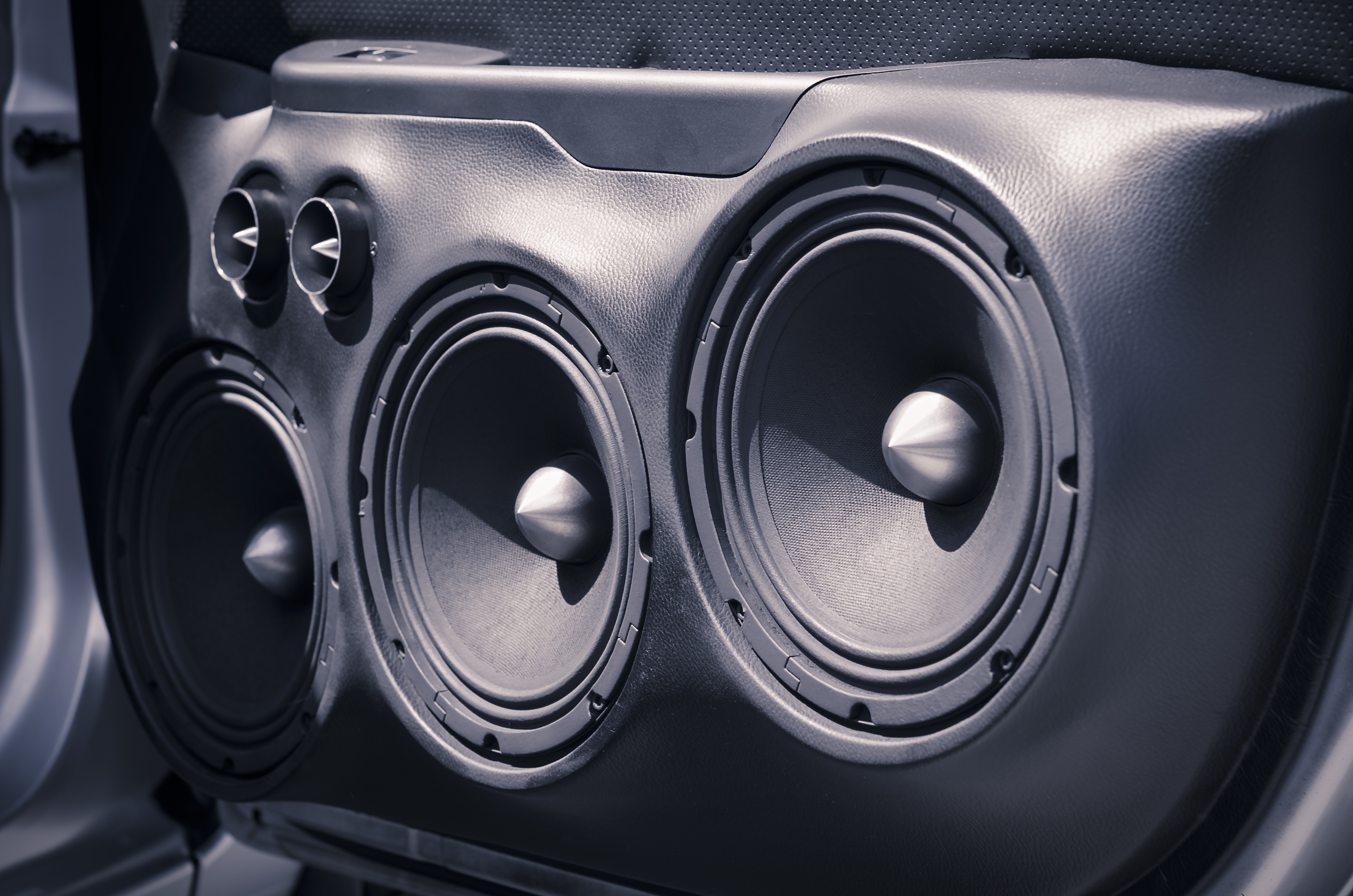 Close view of three woofers and a pair of tweeters mounted in a car door panel with the grilles removed
