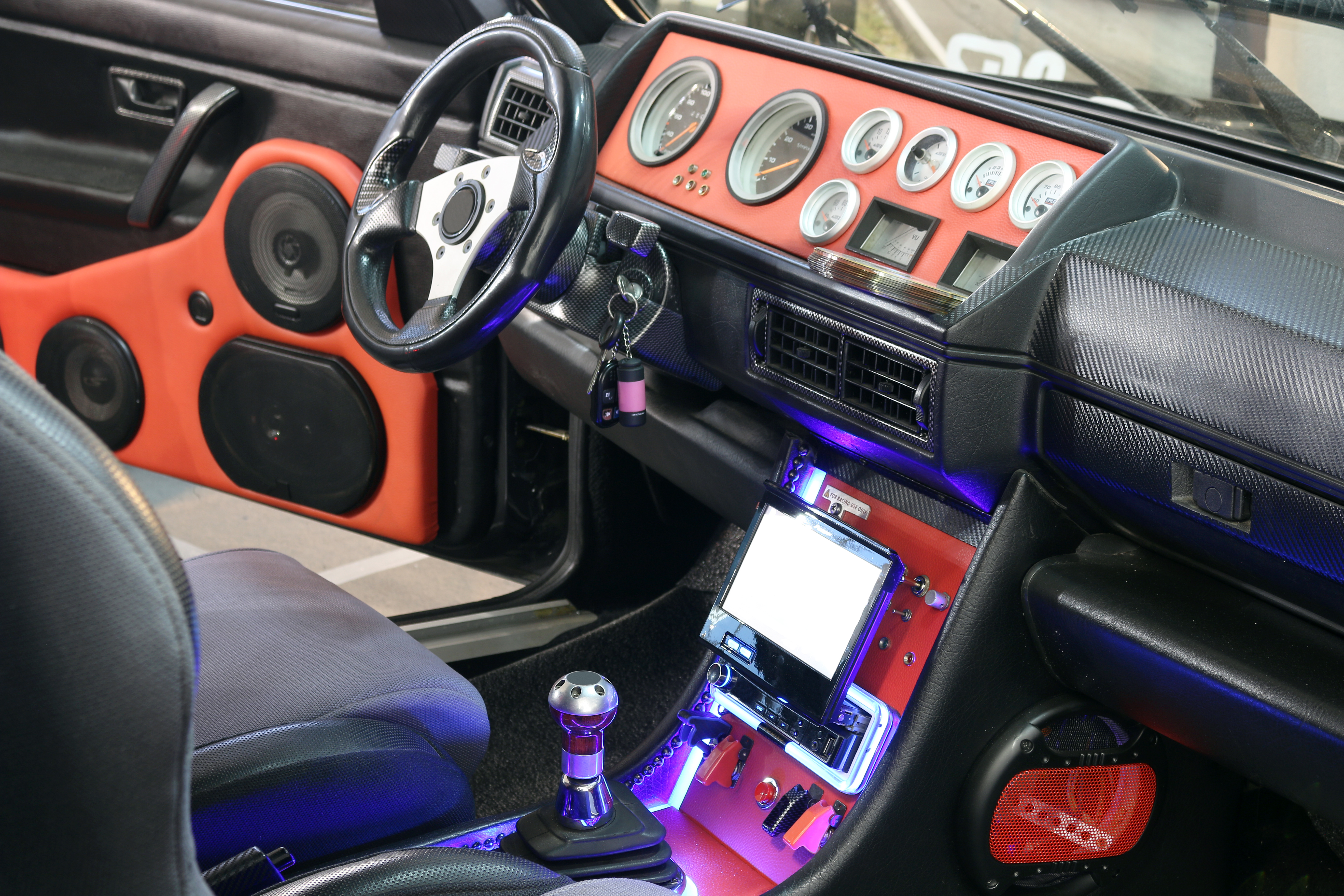 Custom car interior with red door panels holding speakers, a row of round gauges, and blue accent lighting on the console