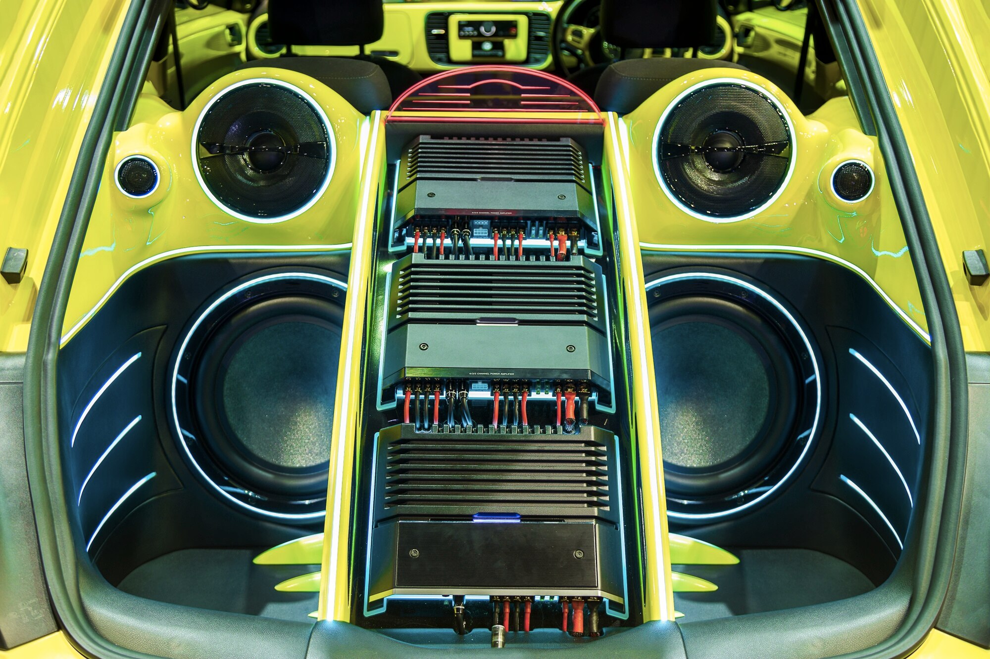 Yellow hatchback trunk build with stacked amplifiers between two large subwoofers and speakers under neon accent lighting
