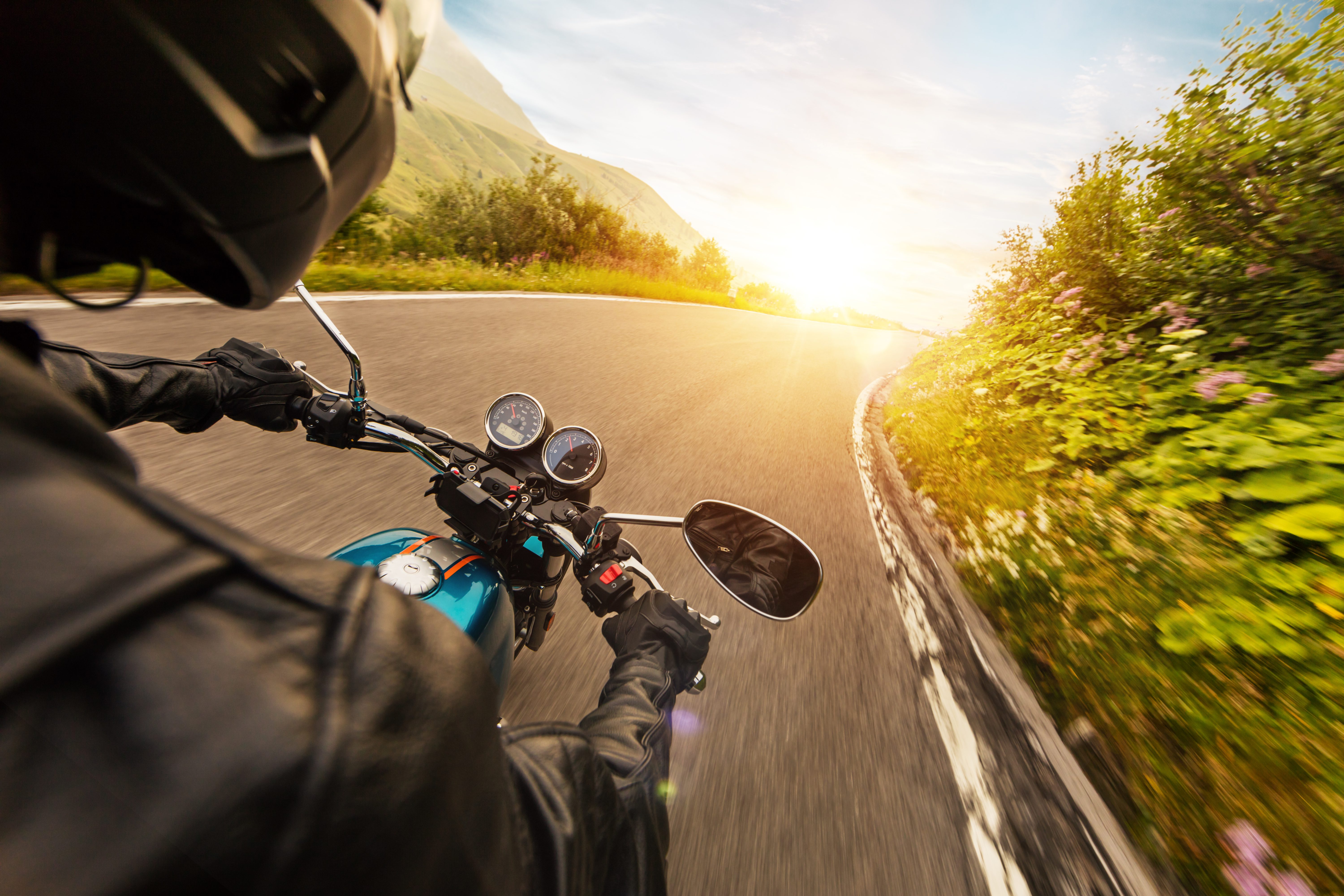 View over a motorcycle rider's shoulder and handlebars while riding a curving country road at sunset