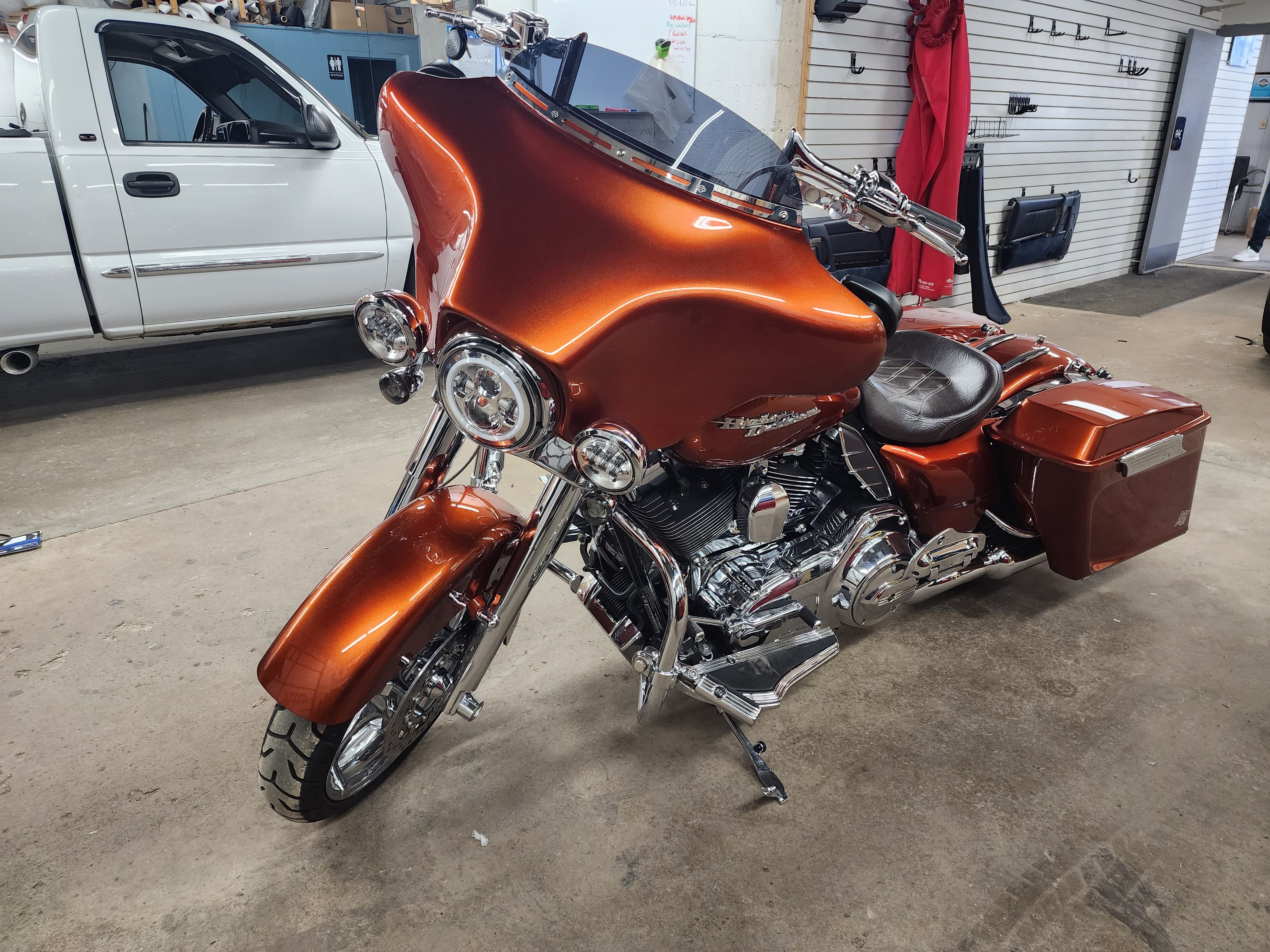 Orange touring motorcycle with a batwing fairing and hard saddlebags parked inside a shop garage