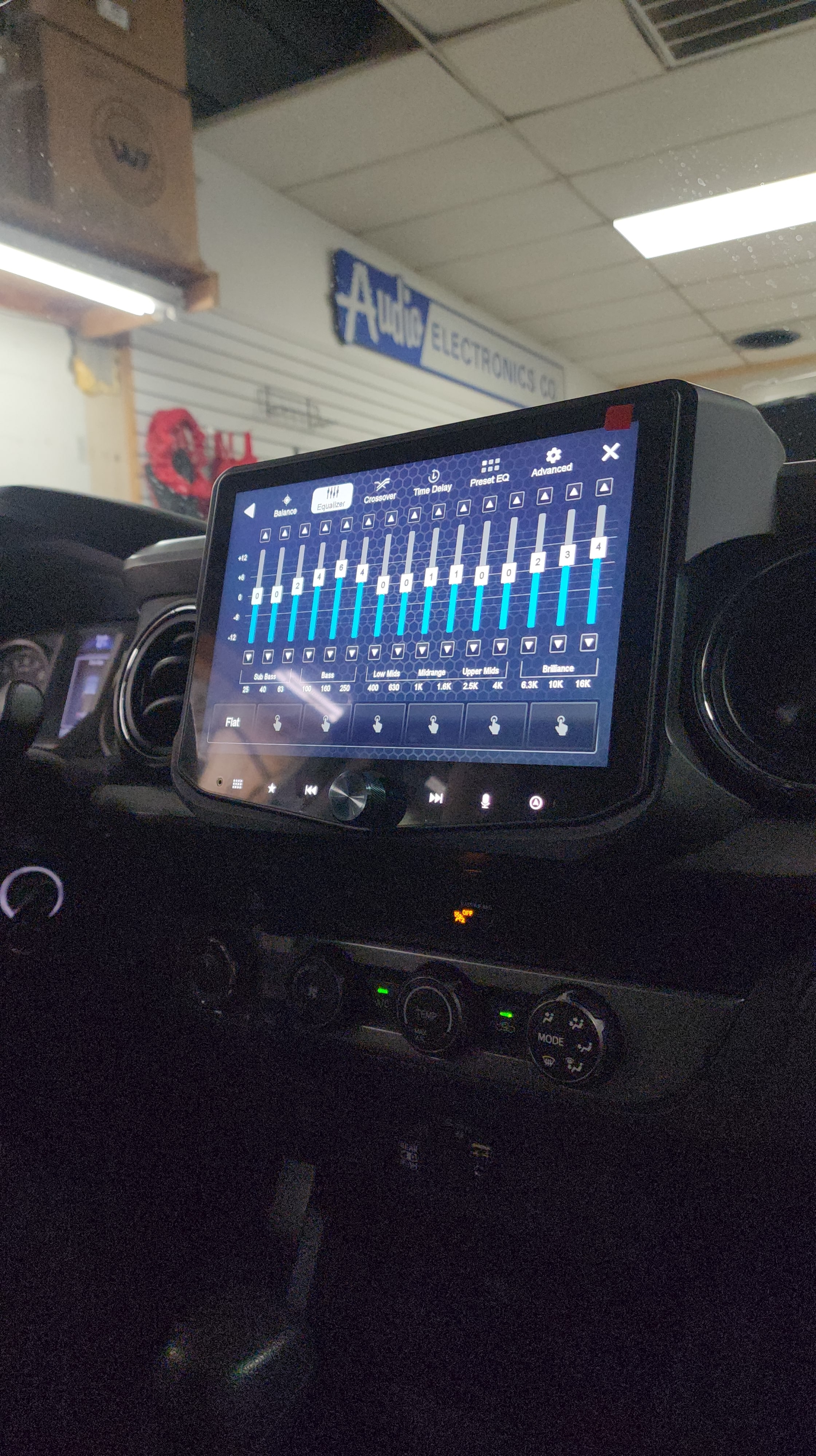Large aftermarket touchscreen stereo installed in a dash showing a multiband equalizer screen inside a shop