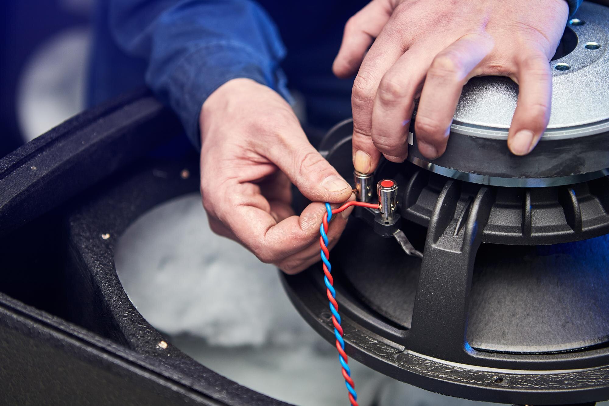 Close view of hands connecting red and black speaker wire to the terminals of a large subwoofer.