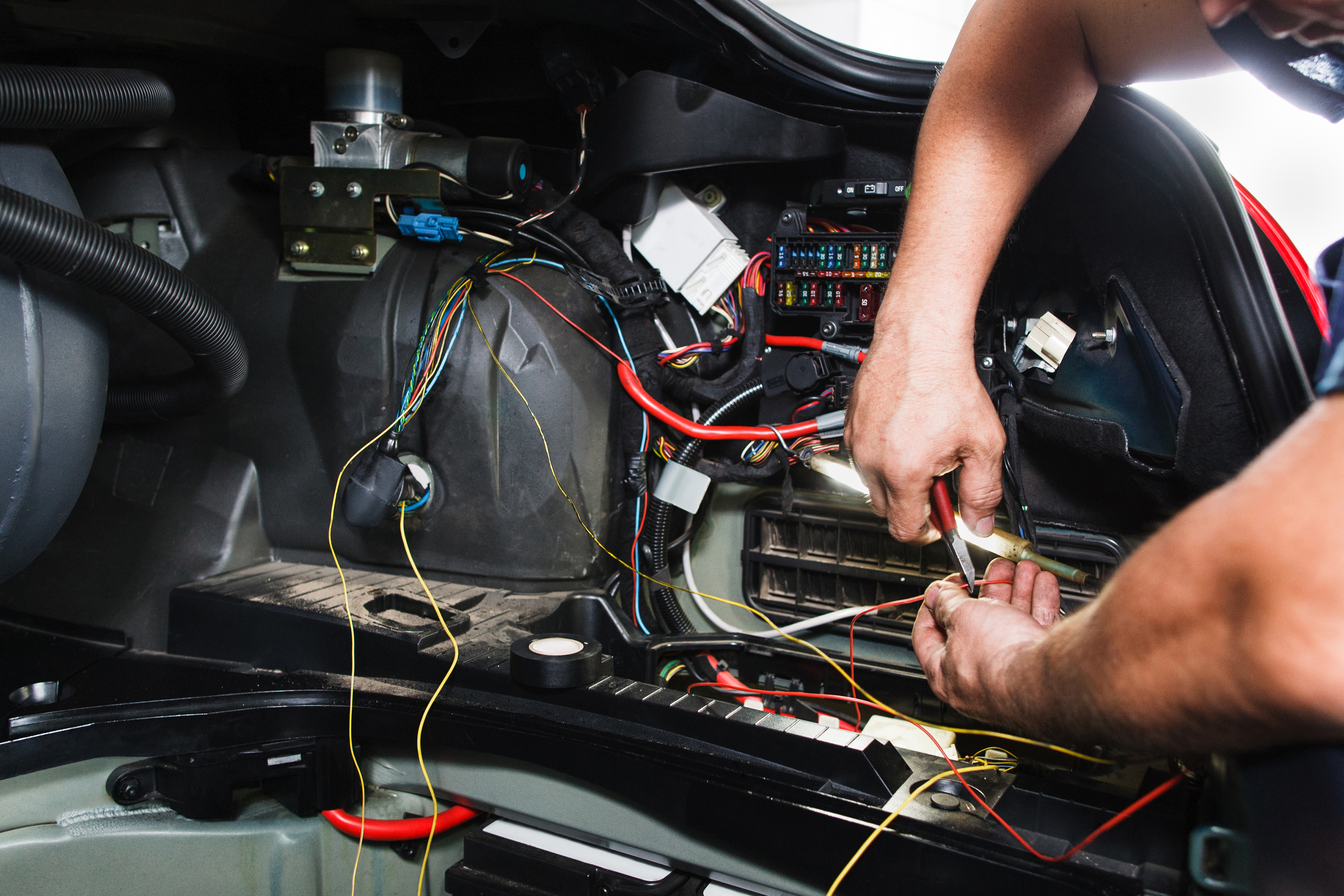 Hands using a tool to connect wires near a vehicle fuse panel under the dash.