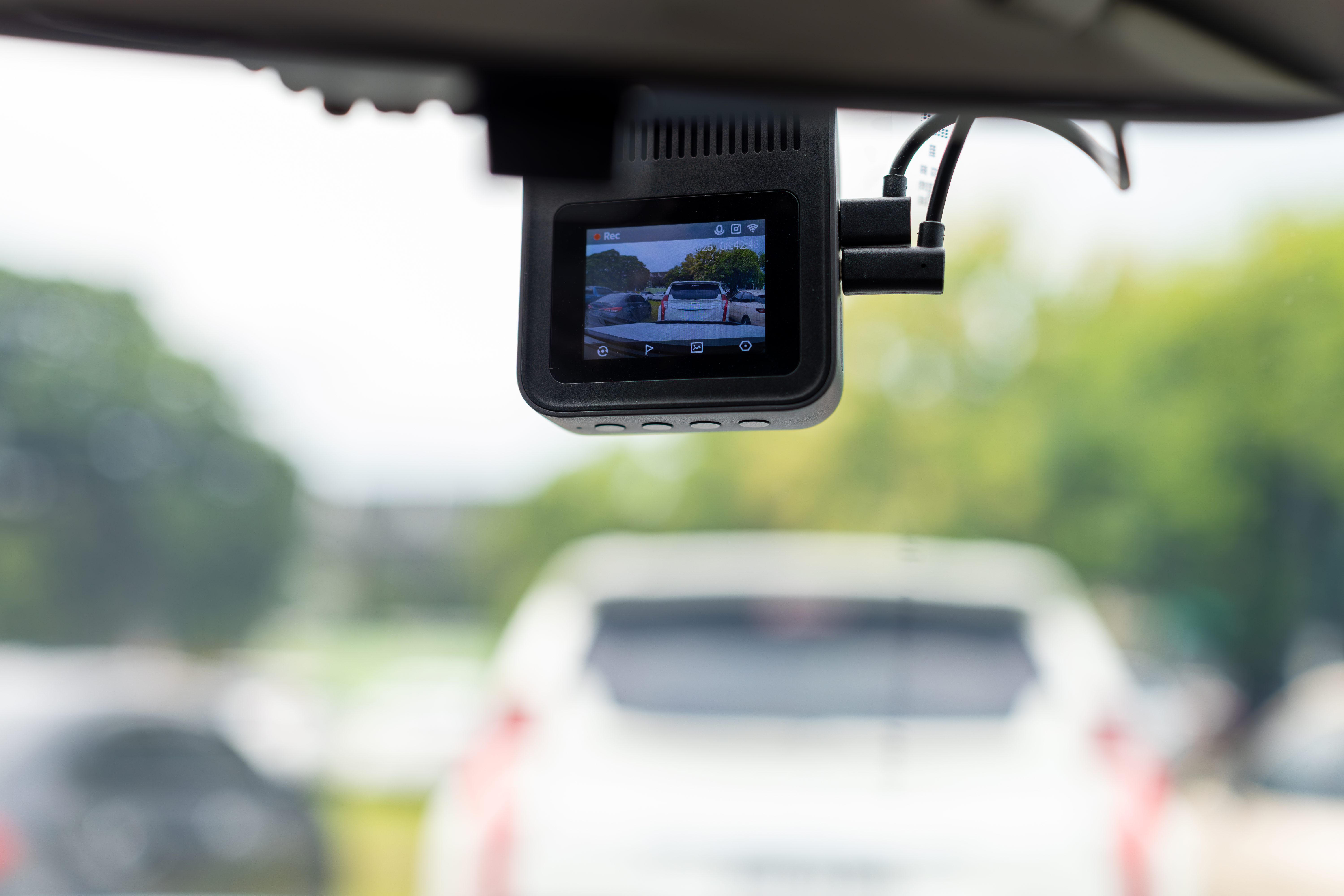 Compact dash camera on a windshield showing the road ahead on its small screen.
