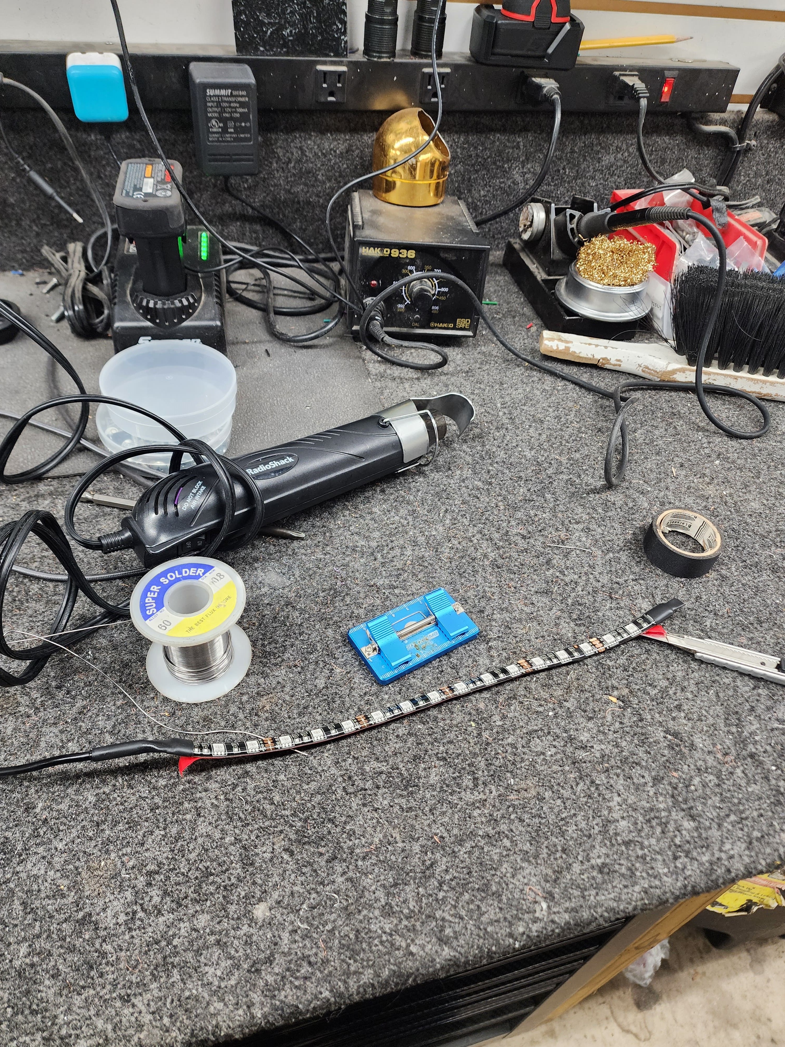 Shop workbench holding a soldering station, heat gun, spool of solder and an addressable LED strip ready for wiring