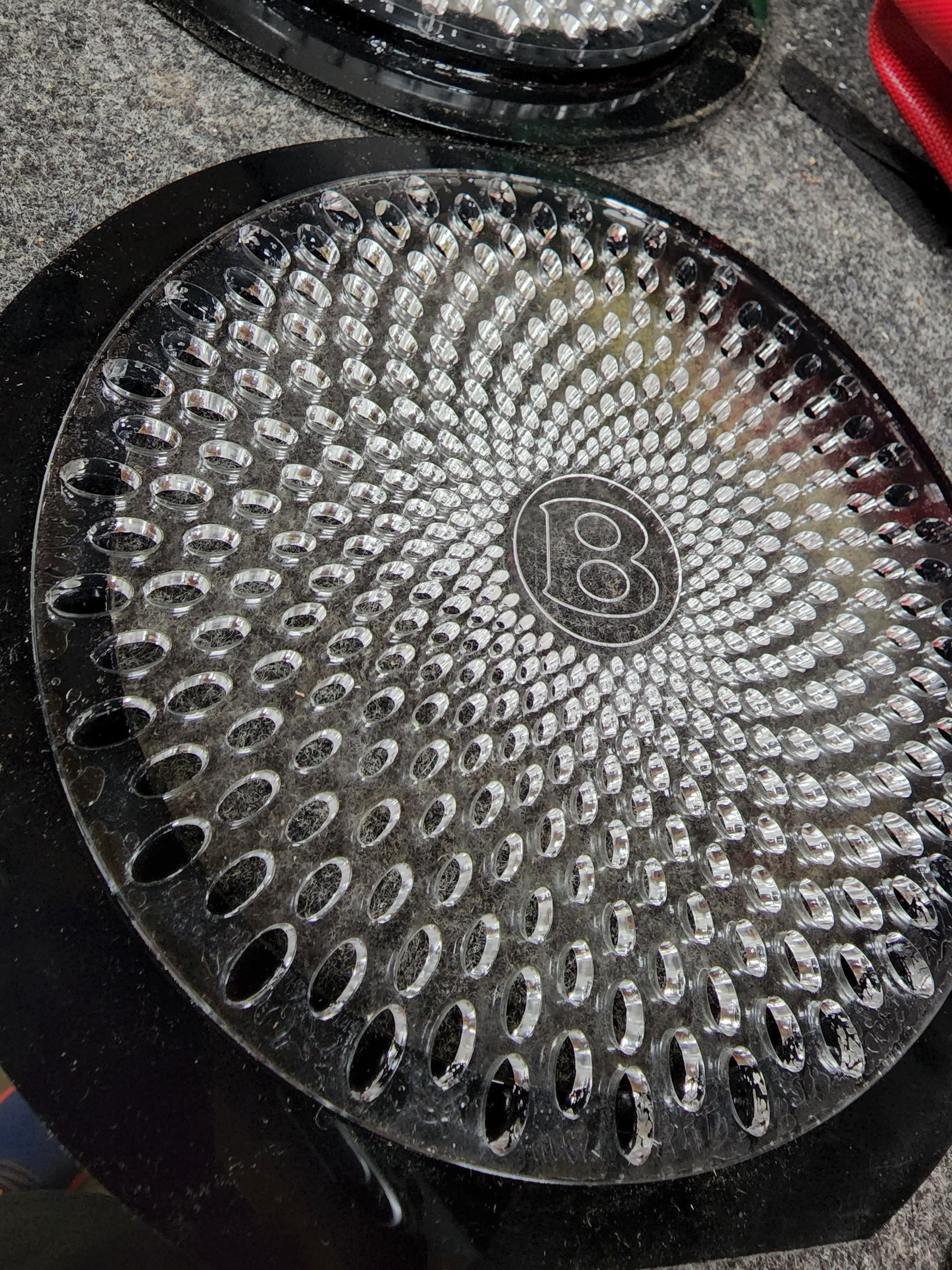 Close view of a polished perforated speaker grille with a circular badge, resting on a workshop surface.