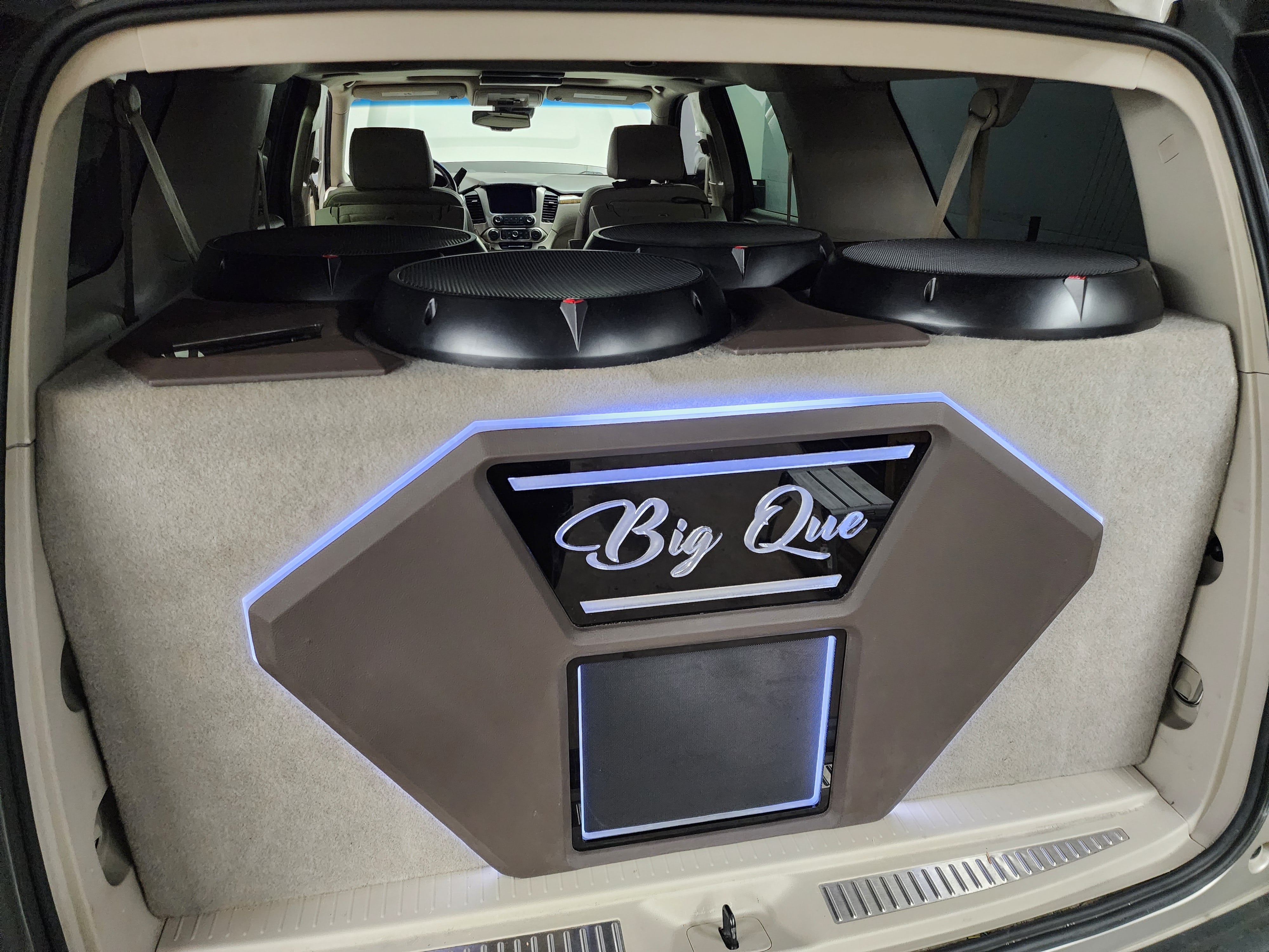 SUV cargo area with four subwoofers mounted across the rear seat back and a lit custom panel with script lettering