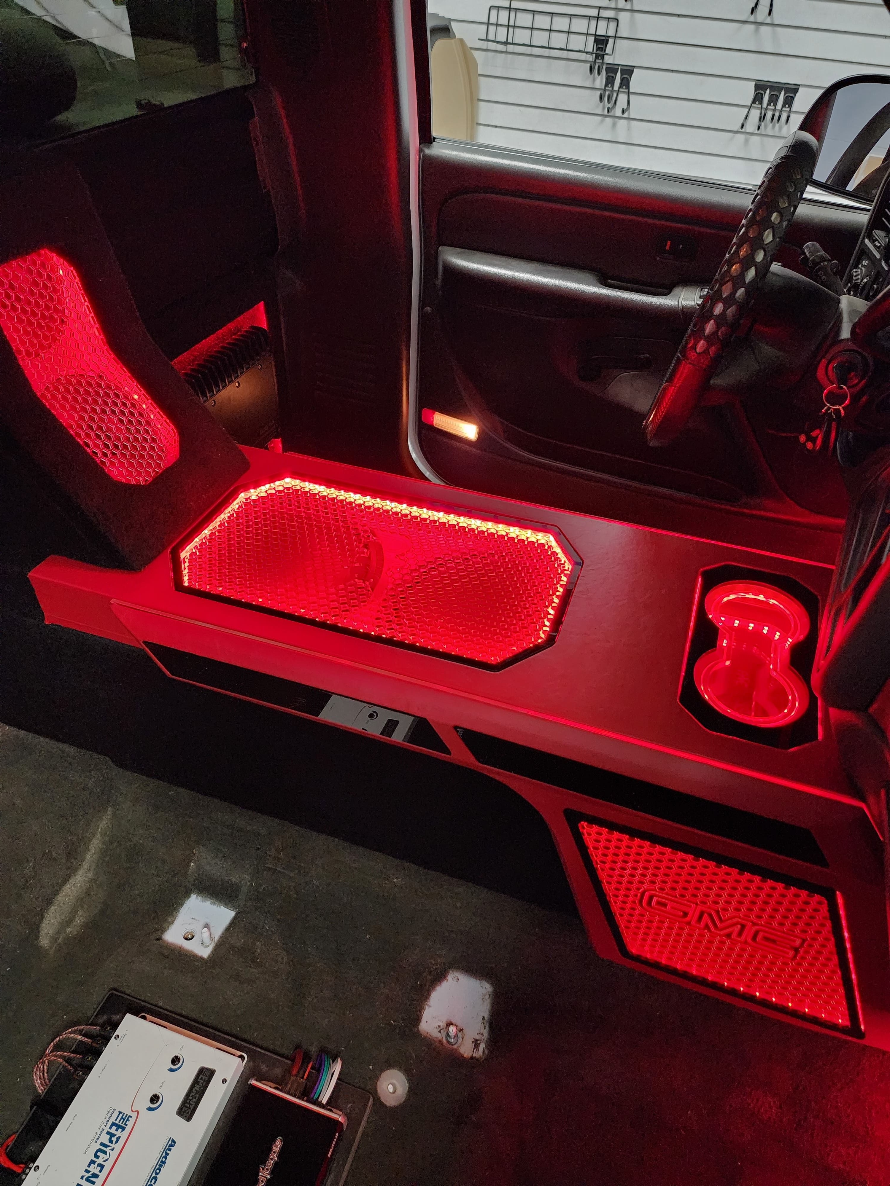 Custom speaker panels and cup holder in a truck cab outlined in bright red accent lighting.