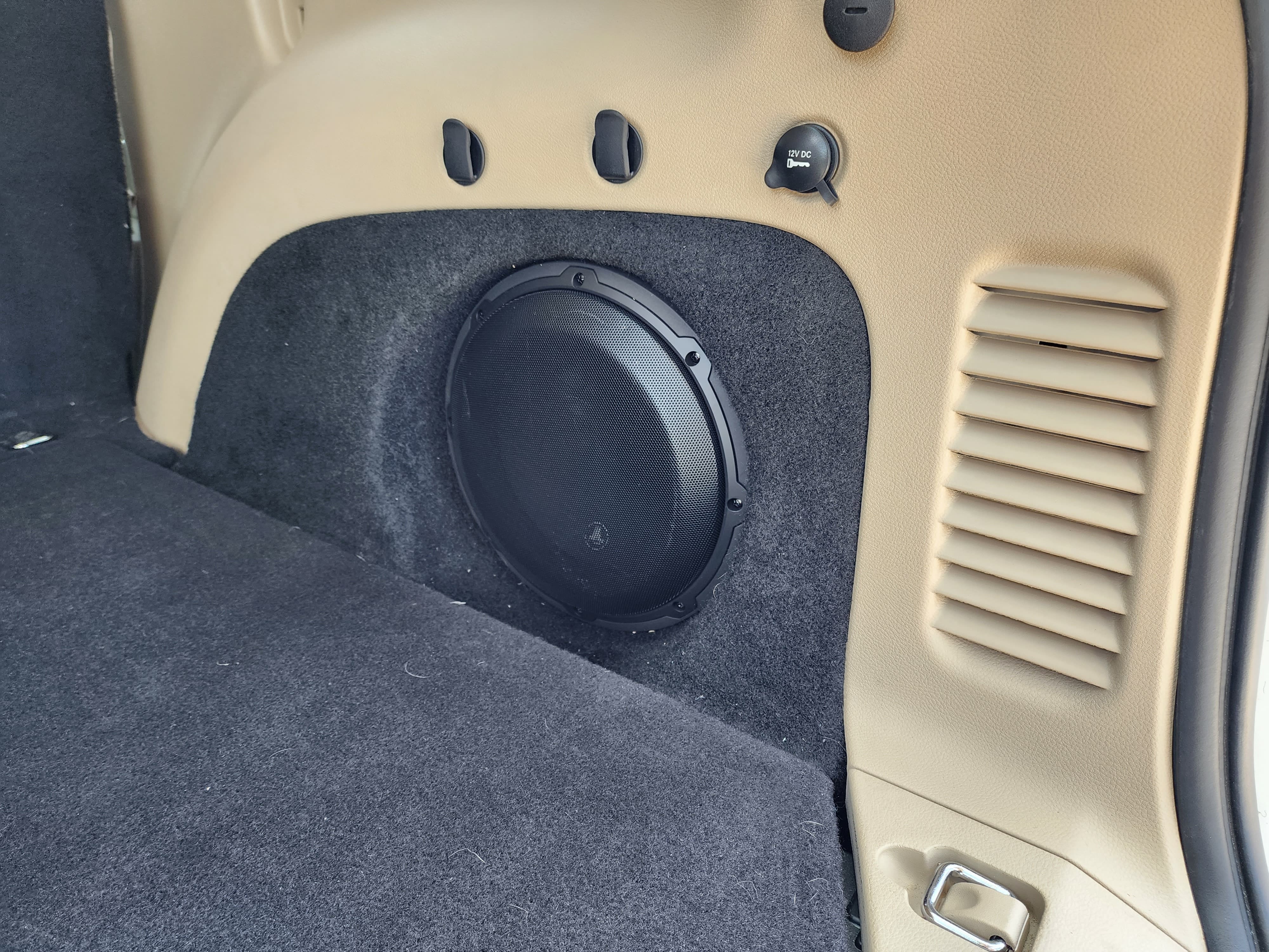 Subwoofer mounted flush into the carpeted rear side panel of an SUV cargo area.