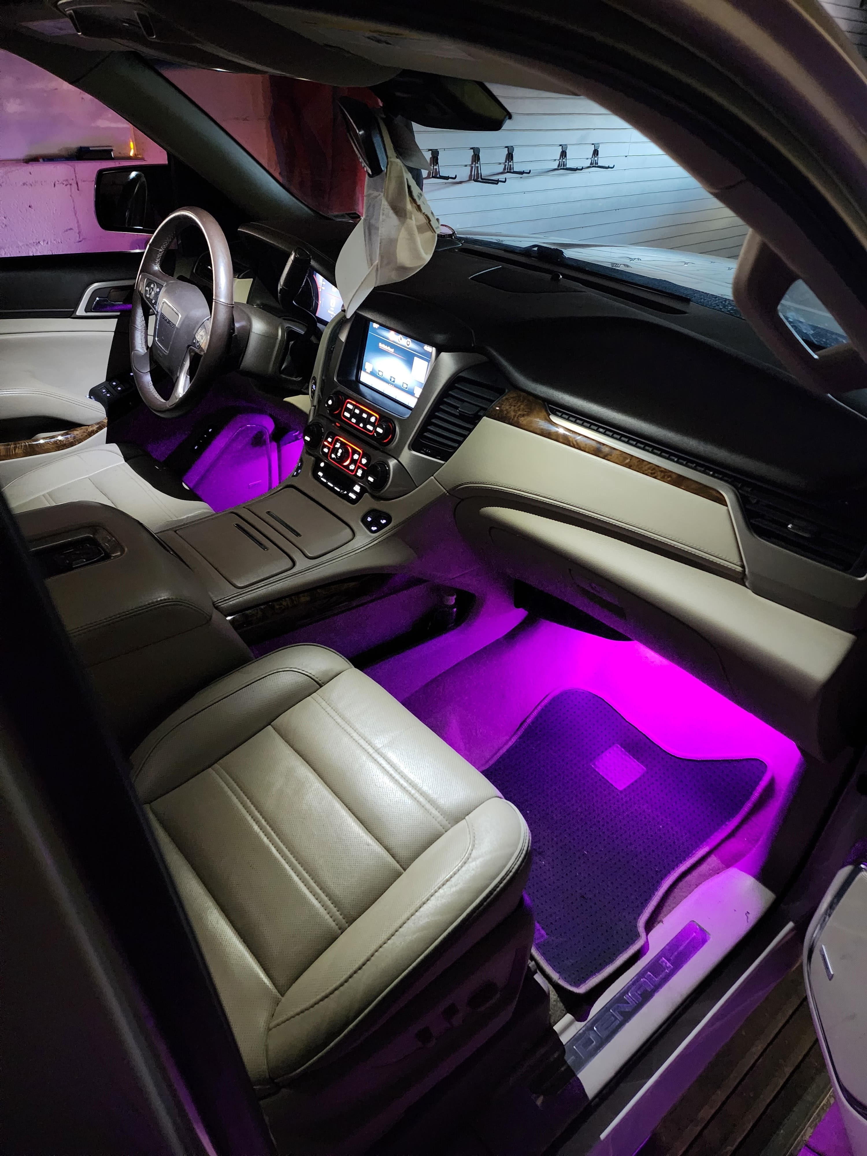 Front passenger area of an SUV with tan leather seats lit by purple LED footwell and dash lighting.