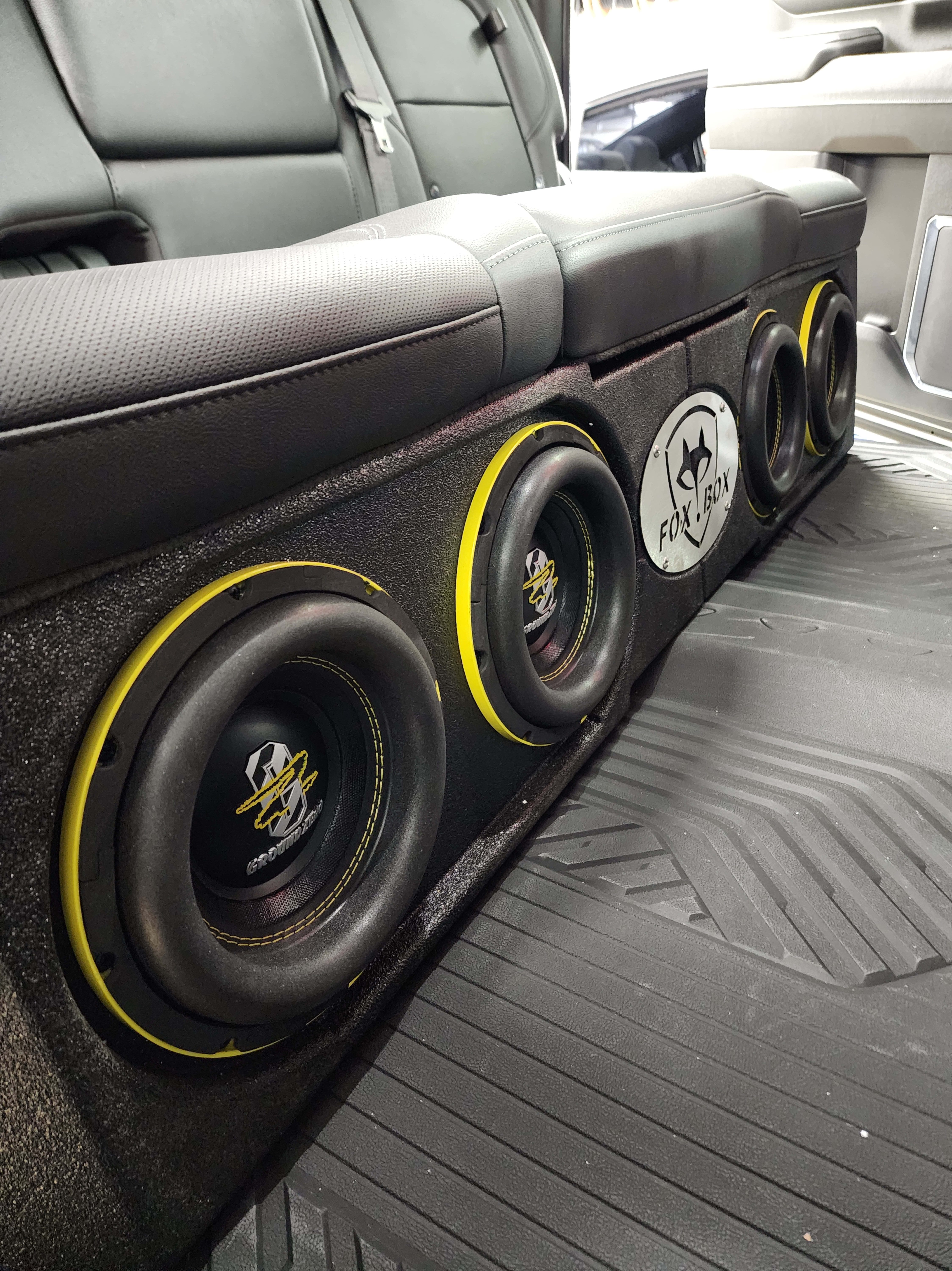 Bank of four subwoofers in a carpeted box running behind the rear seat of a truck