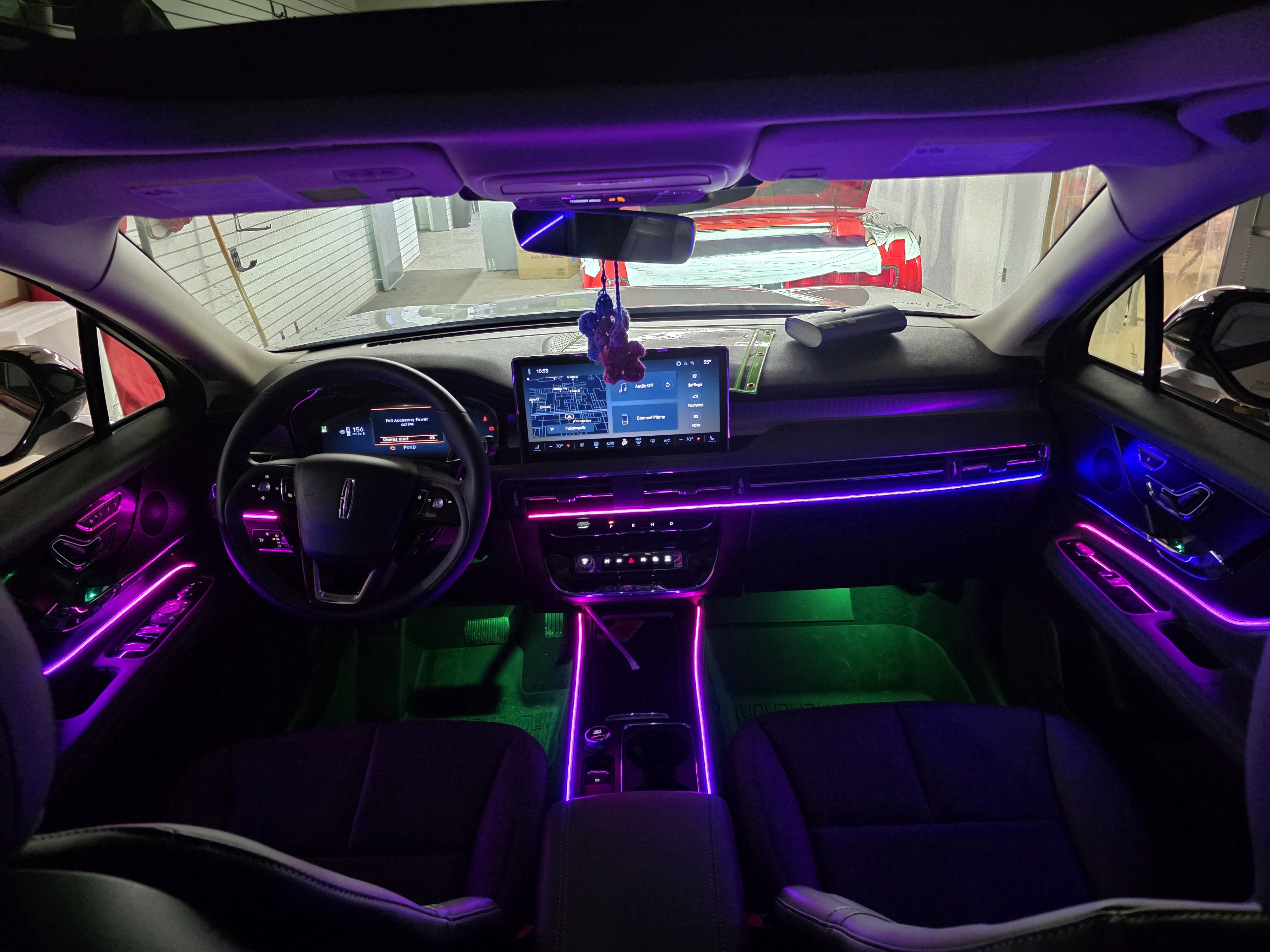 Car interior lit by purple and green ambient LED strips running across the dash, doors and footwells at night