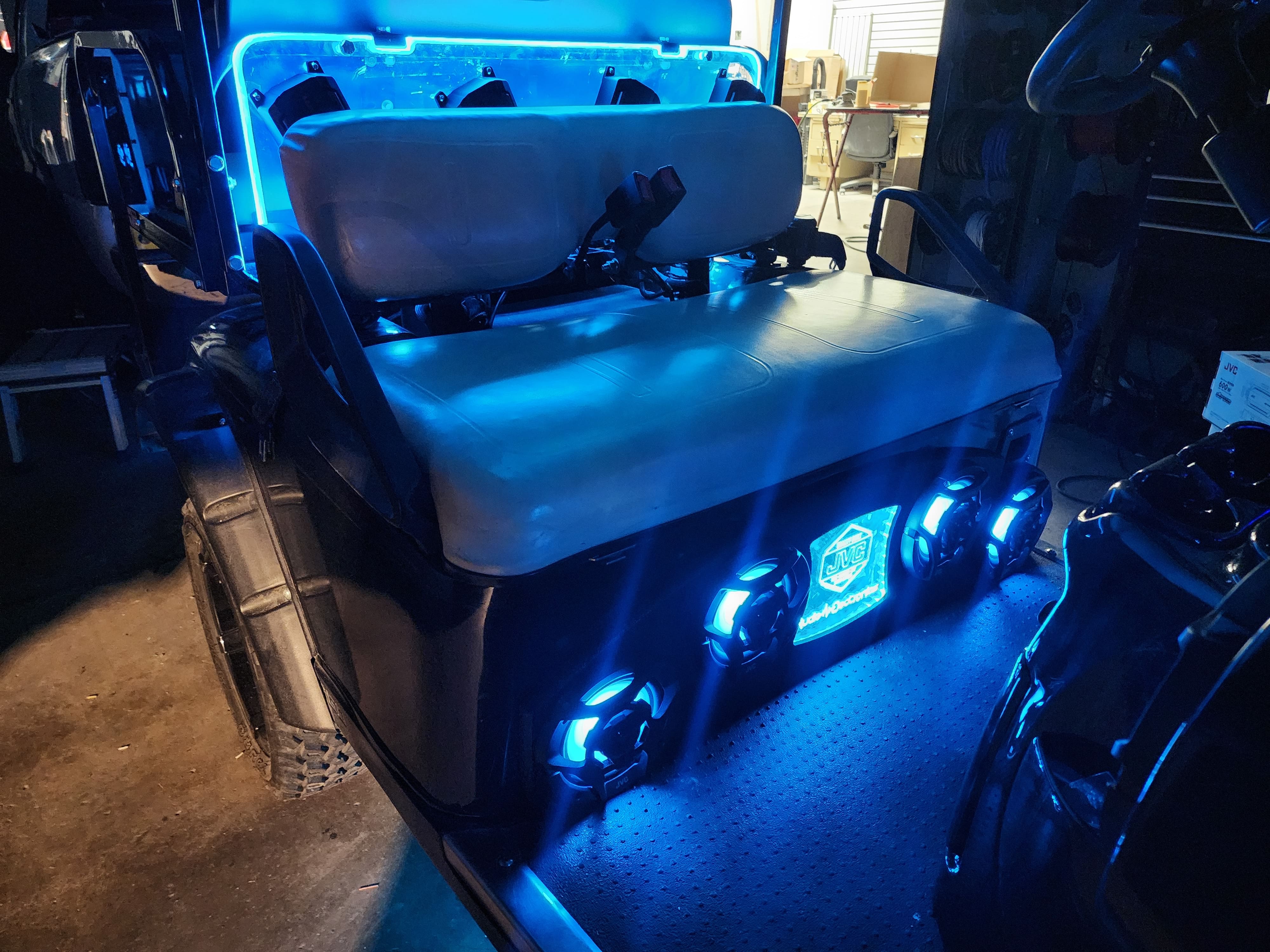 Golf cart fitted with several speakers ringed by blue LEDs and a blue lit roof bar, parked inside a shop