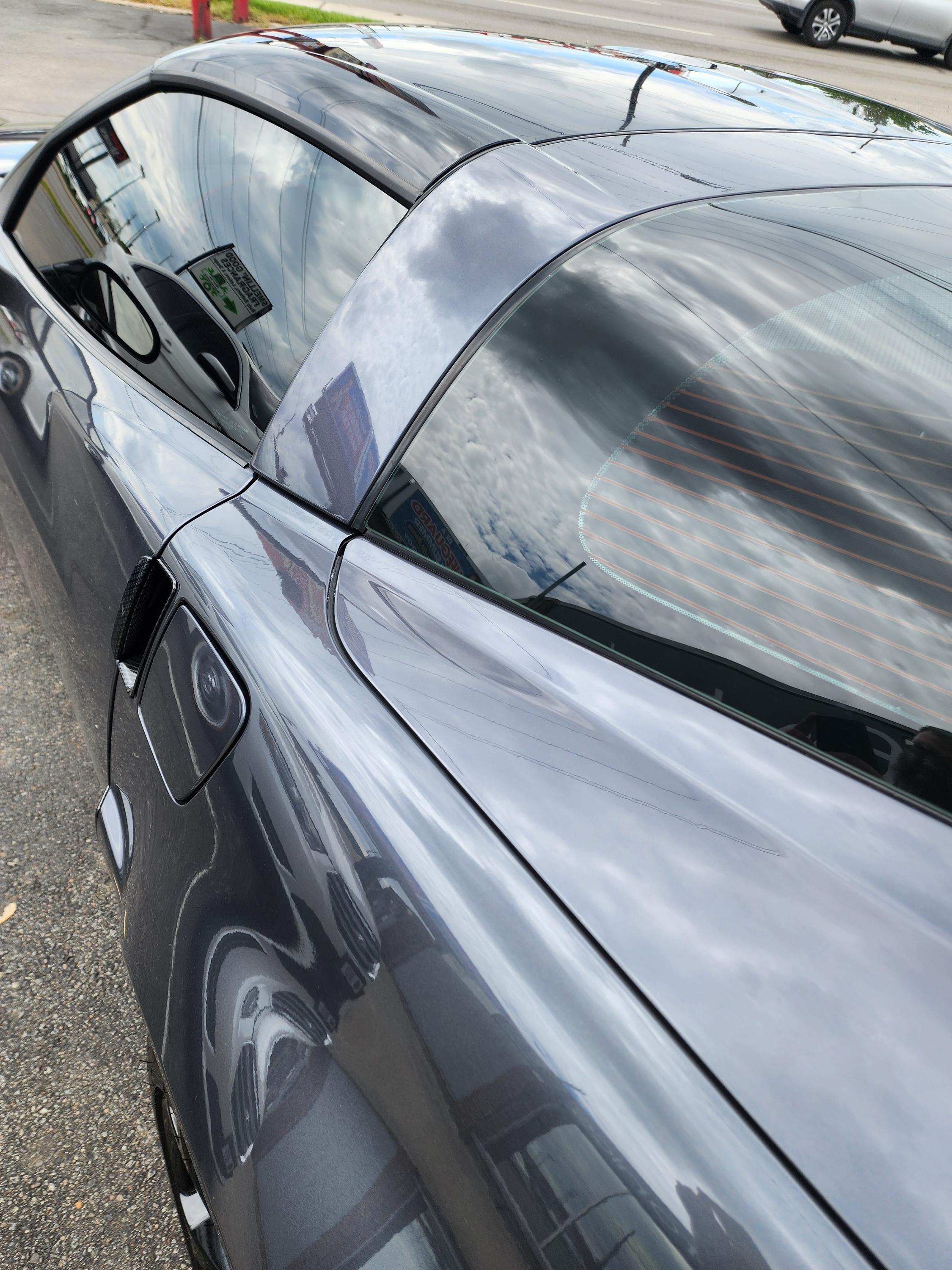 Tinted rear side glass and back window on a gray coupe, with sky and clouds mirrored in the paint.