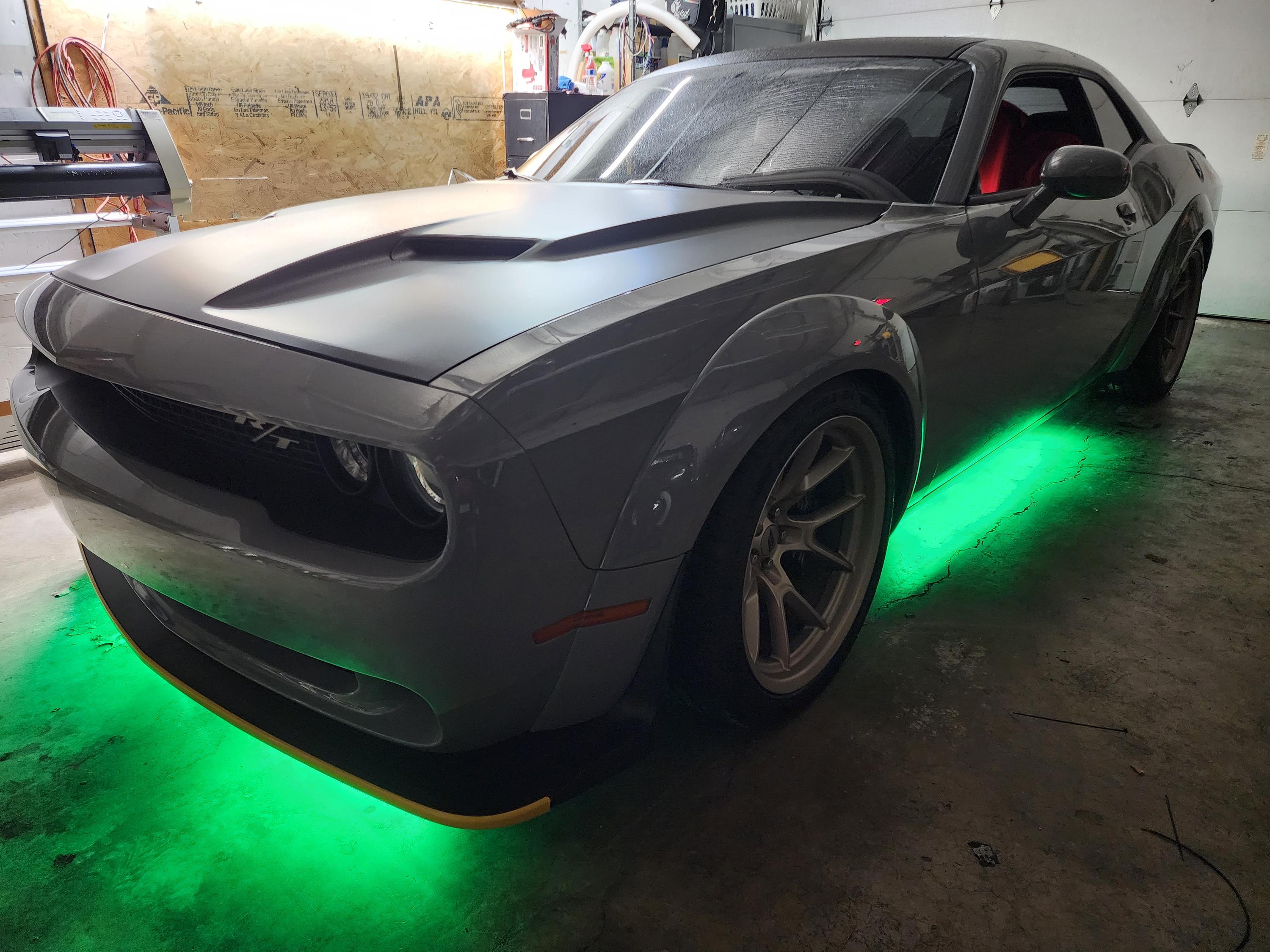 Gray muscle car in a shop bay with green LED underglow lighting the floor beneath its body.