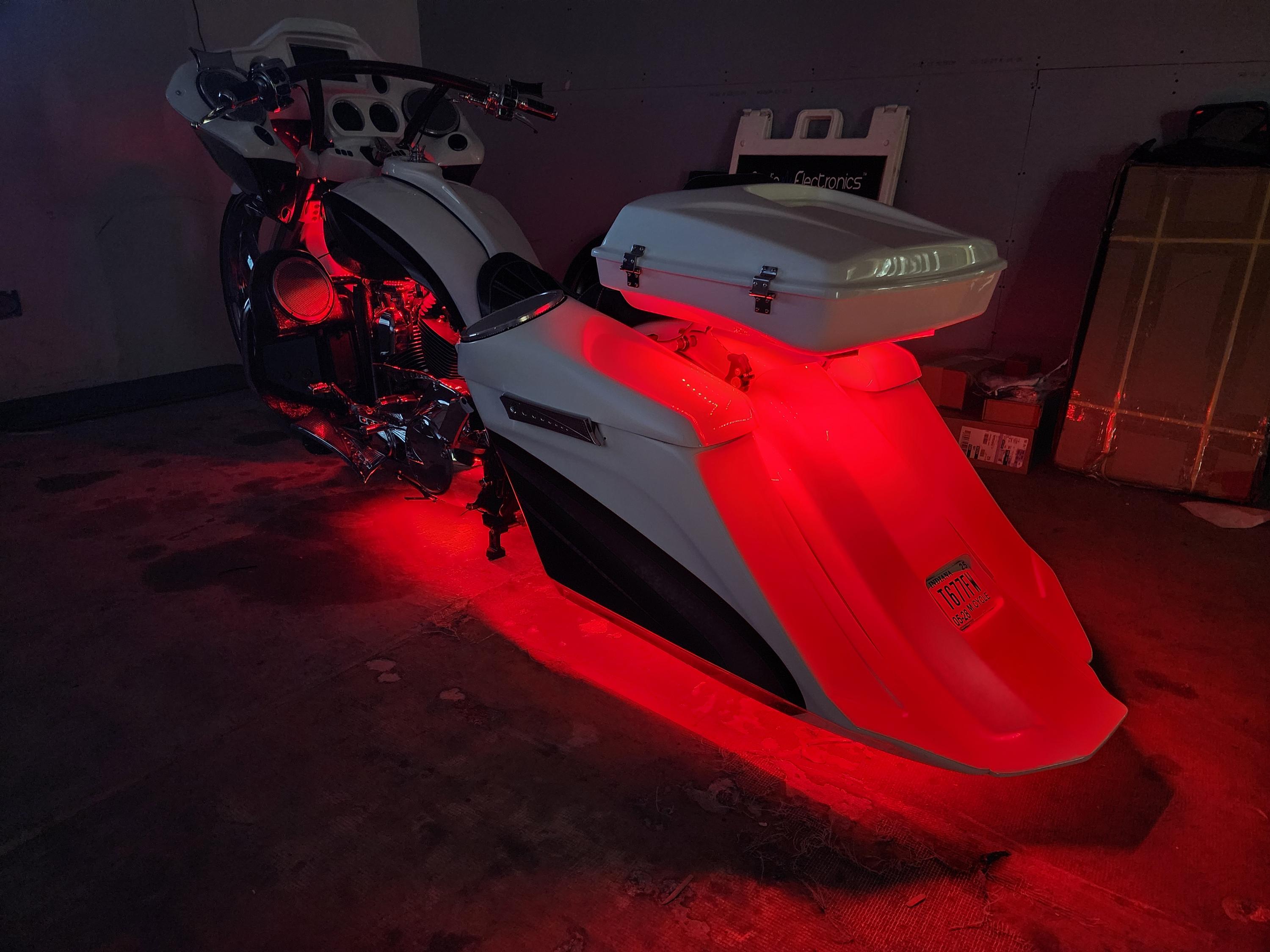 White touring motorcycle with red accent lighting glowing under the saddlebags and engine in a dim garage.