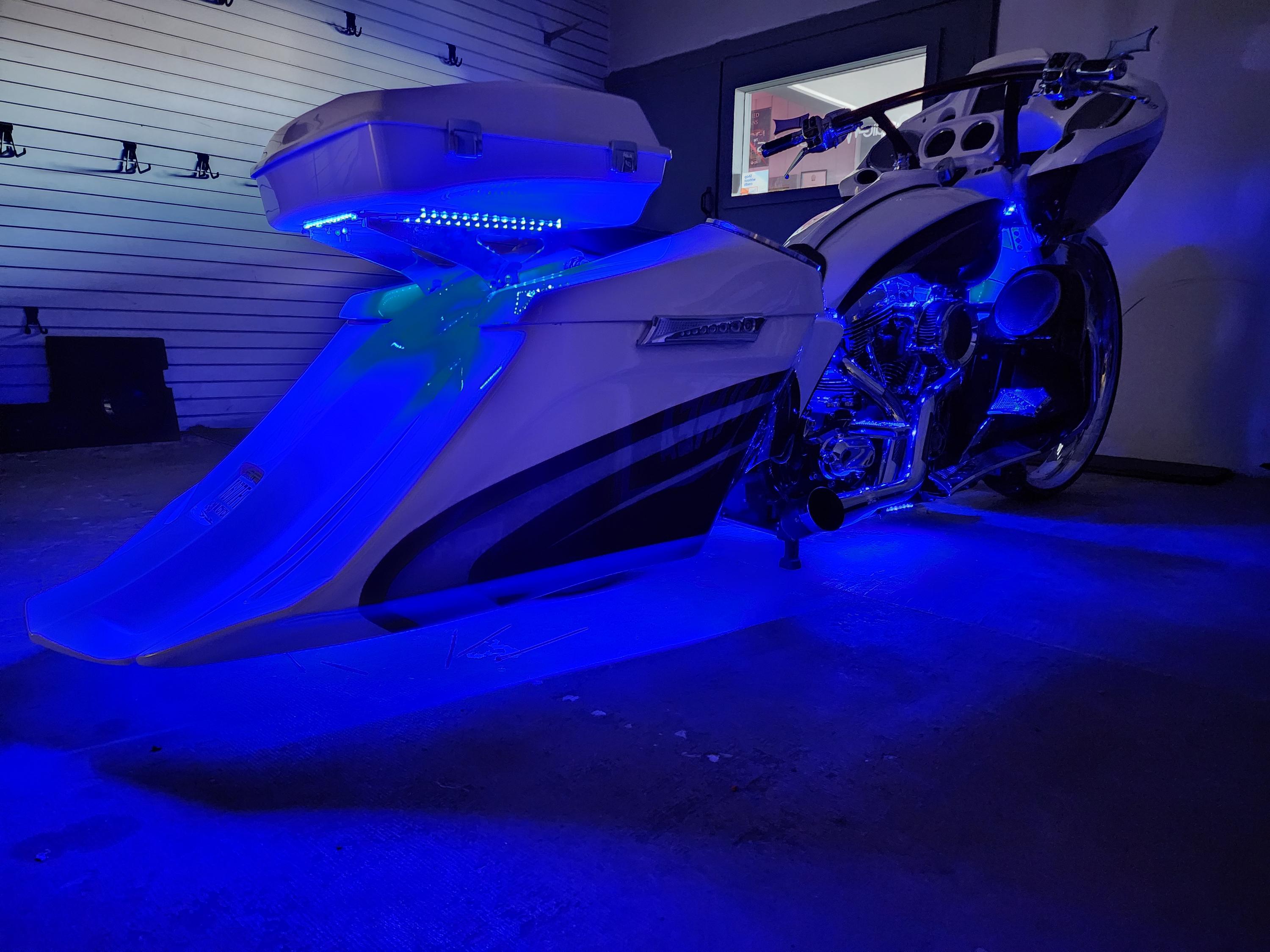 White custom bagger motorcycle lit from below by blue LED accent lighting inside a shop.