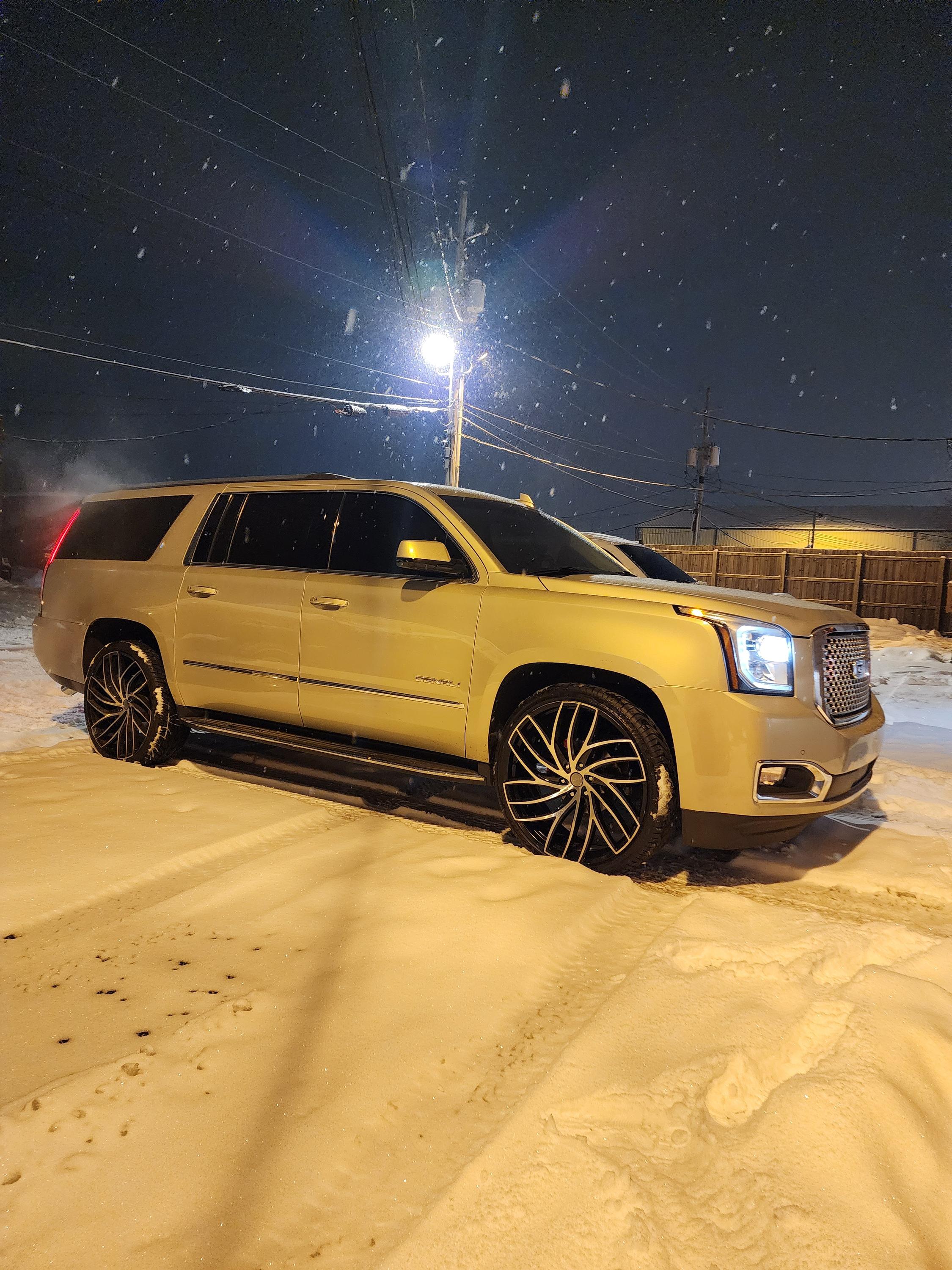 Full size SUV with dark tinted windows parked on packed snow at night under a bright street light.