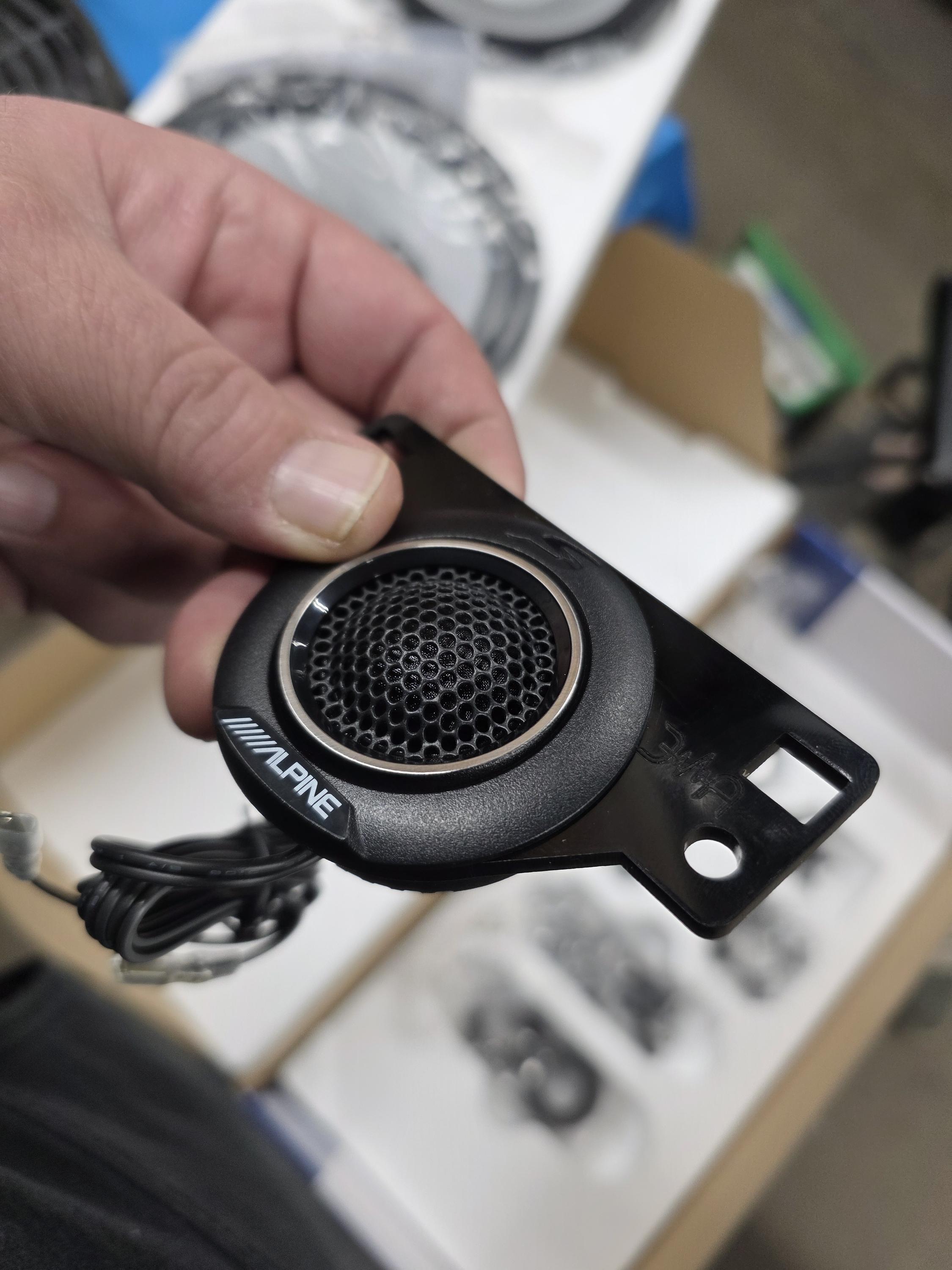 Hand holding a small tweeter in a molded mounting bracket with its wire above an open parts box